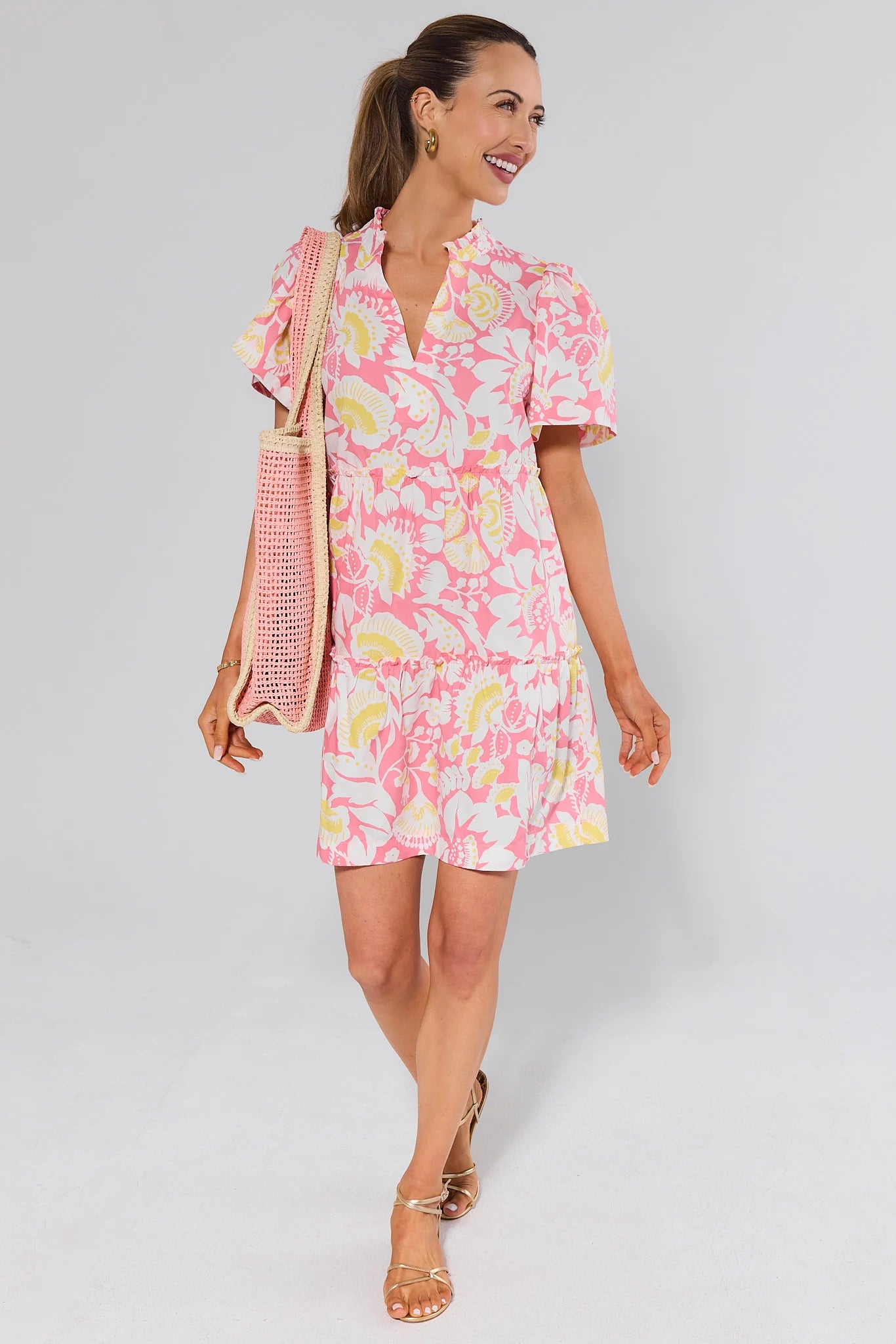 Woman wearing a pink floral dress and bag with a white background