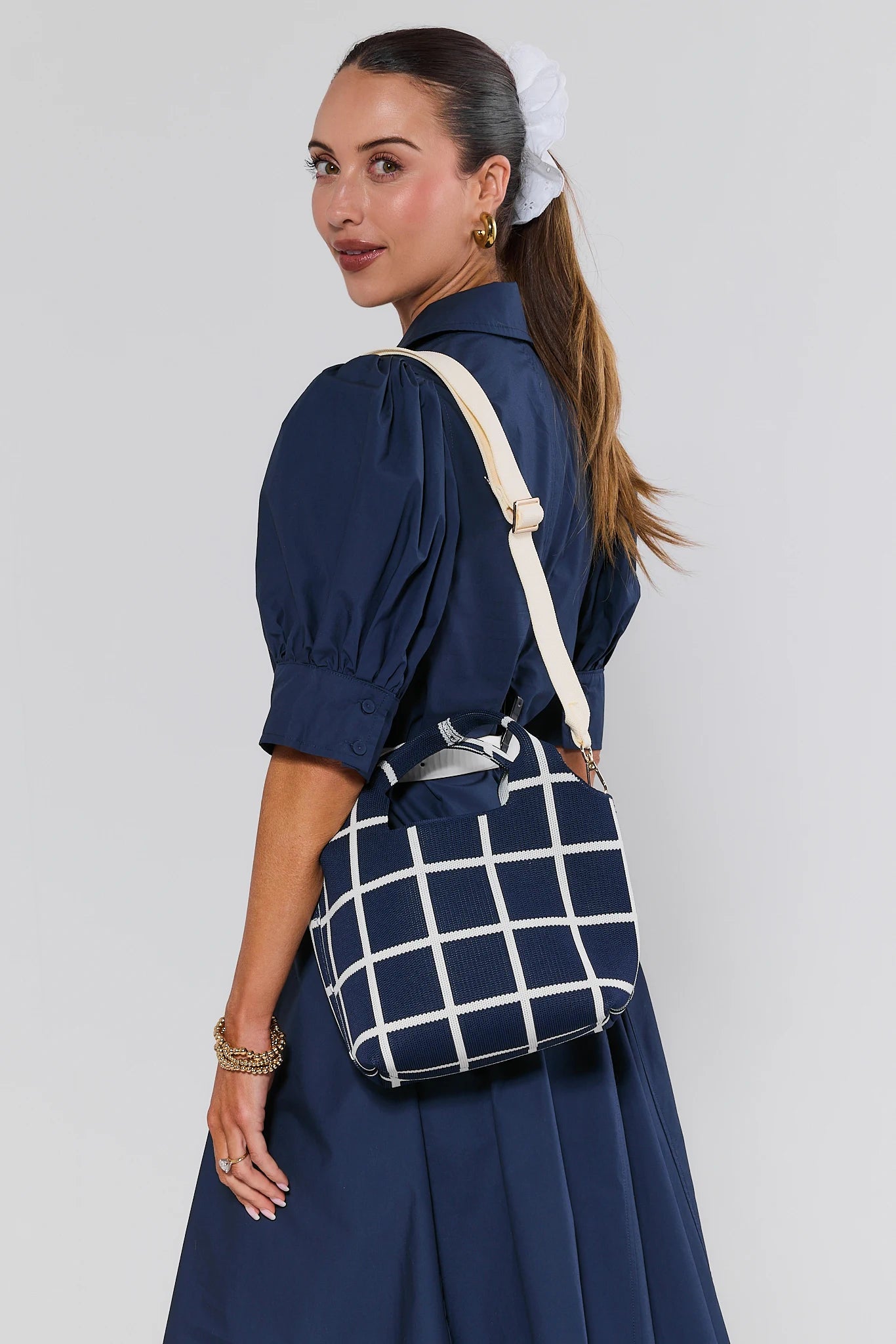 Woman wearing a navy blue dress with a white grid-patterned bag on a plain background