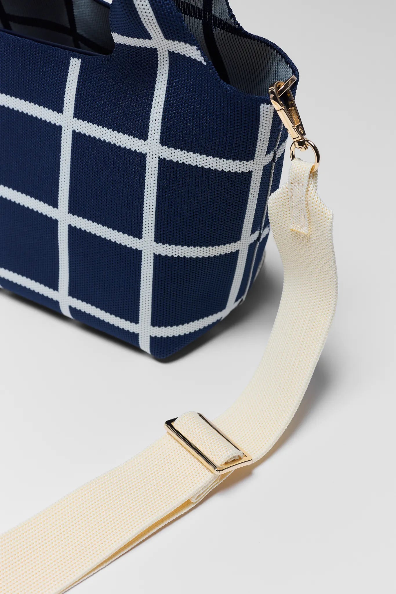 Navy blue bag with white grid pattern and beige strap on a light gray background