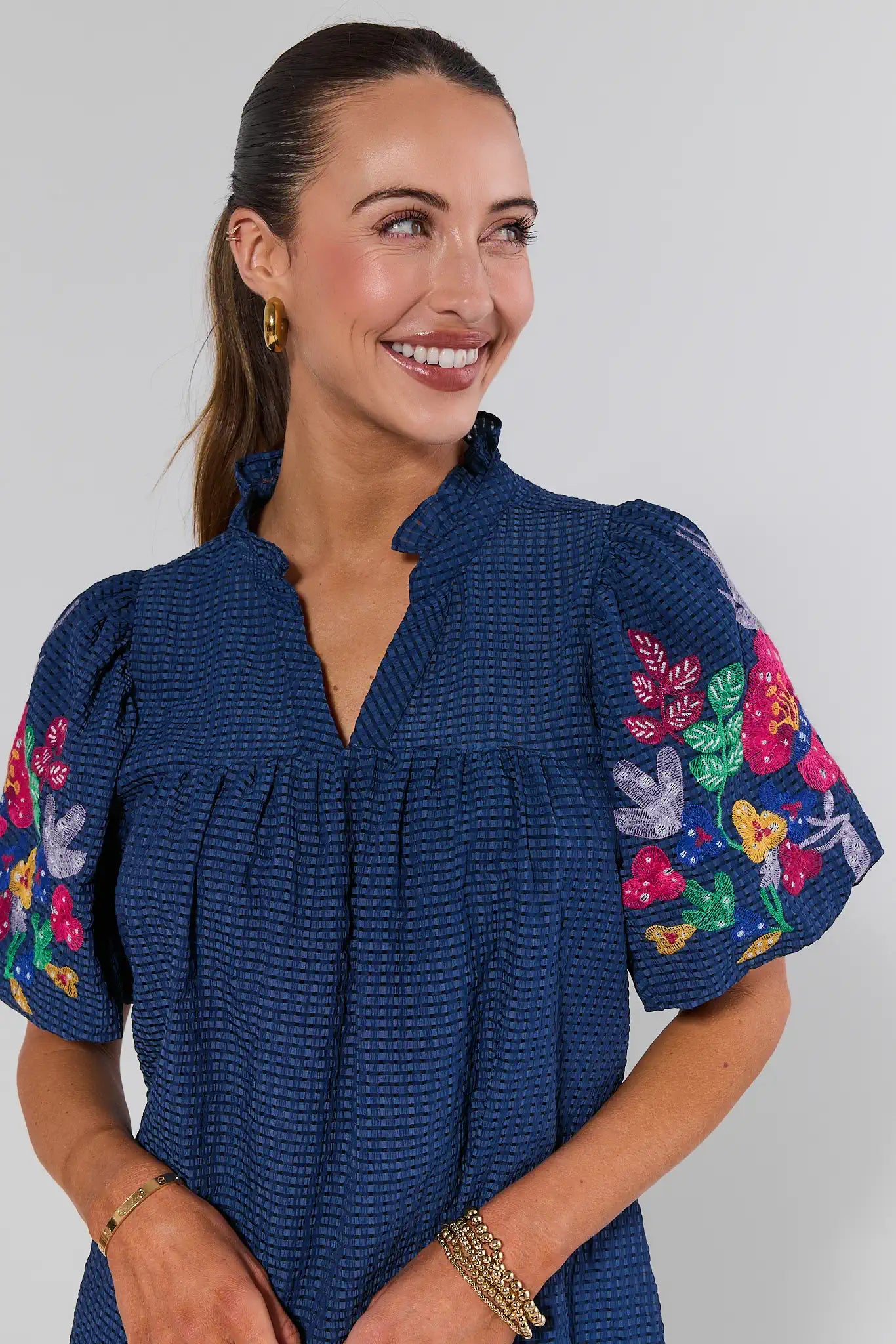 Woman wearing a blue dress with colorful floral embroidery on a plain background