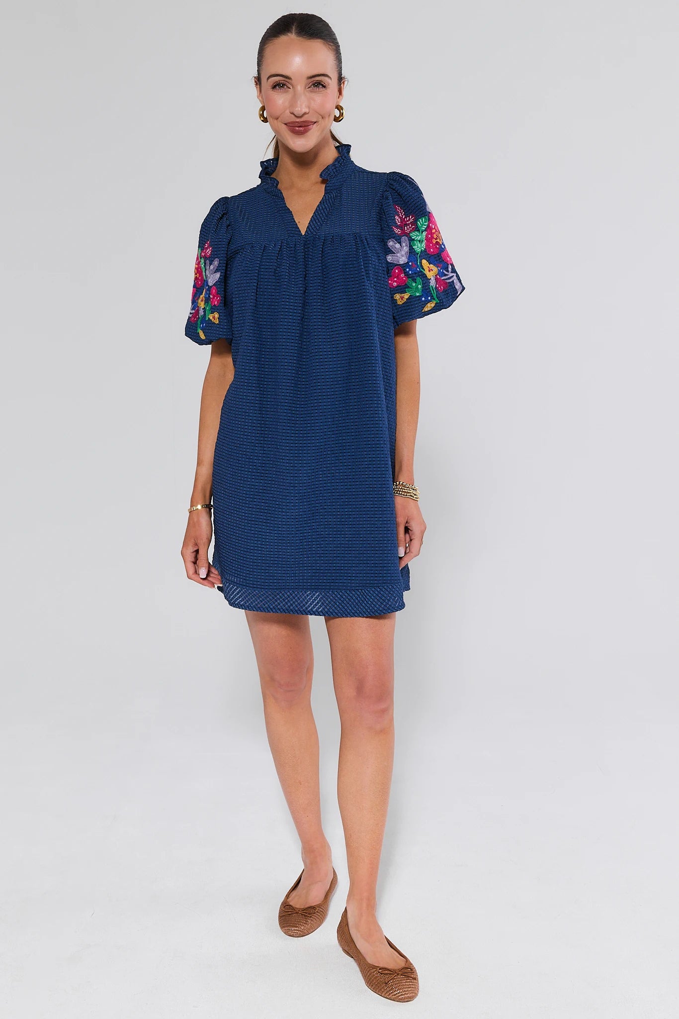 Woman wearing a blue dress with colorful floral embroidery on sleeves against a white background