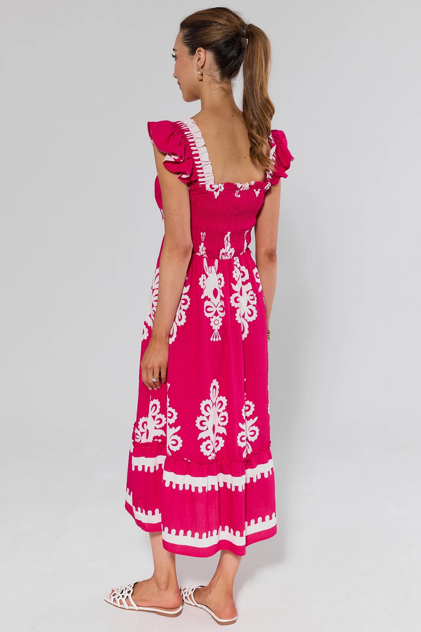 Woman standing wearing a pink dress with white patterns on a gray background