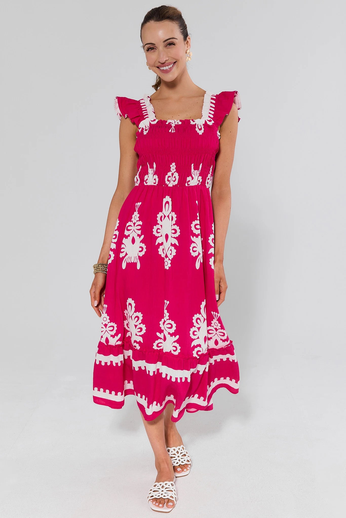 Woman wearing a pink dress with white patterns and sandals on a gray background