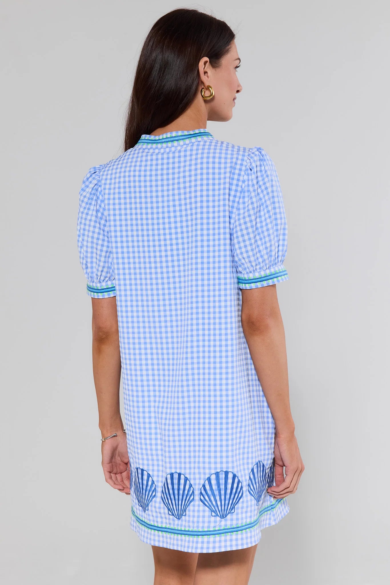 Woman standing wearing a blue and white checkered dress with shell patterns on a plain background