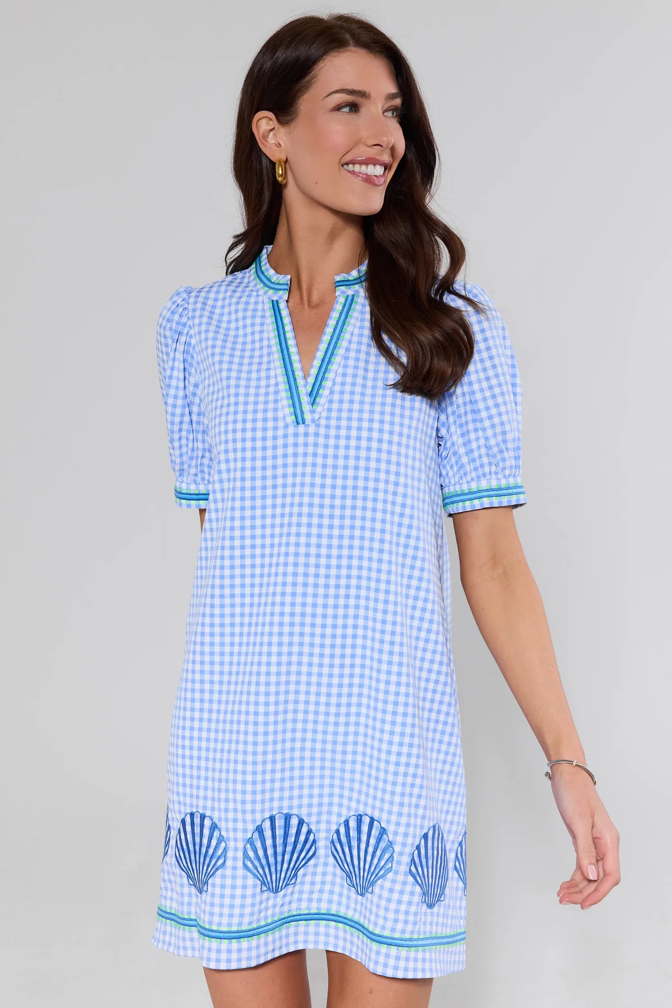 Woman wearing a blue checkered dress with shell patterns on a plain background