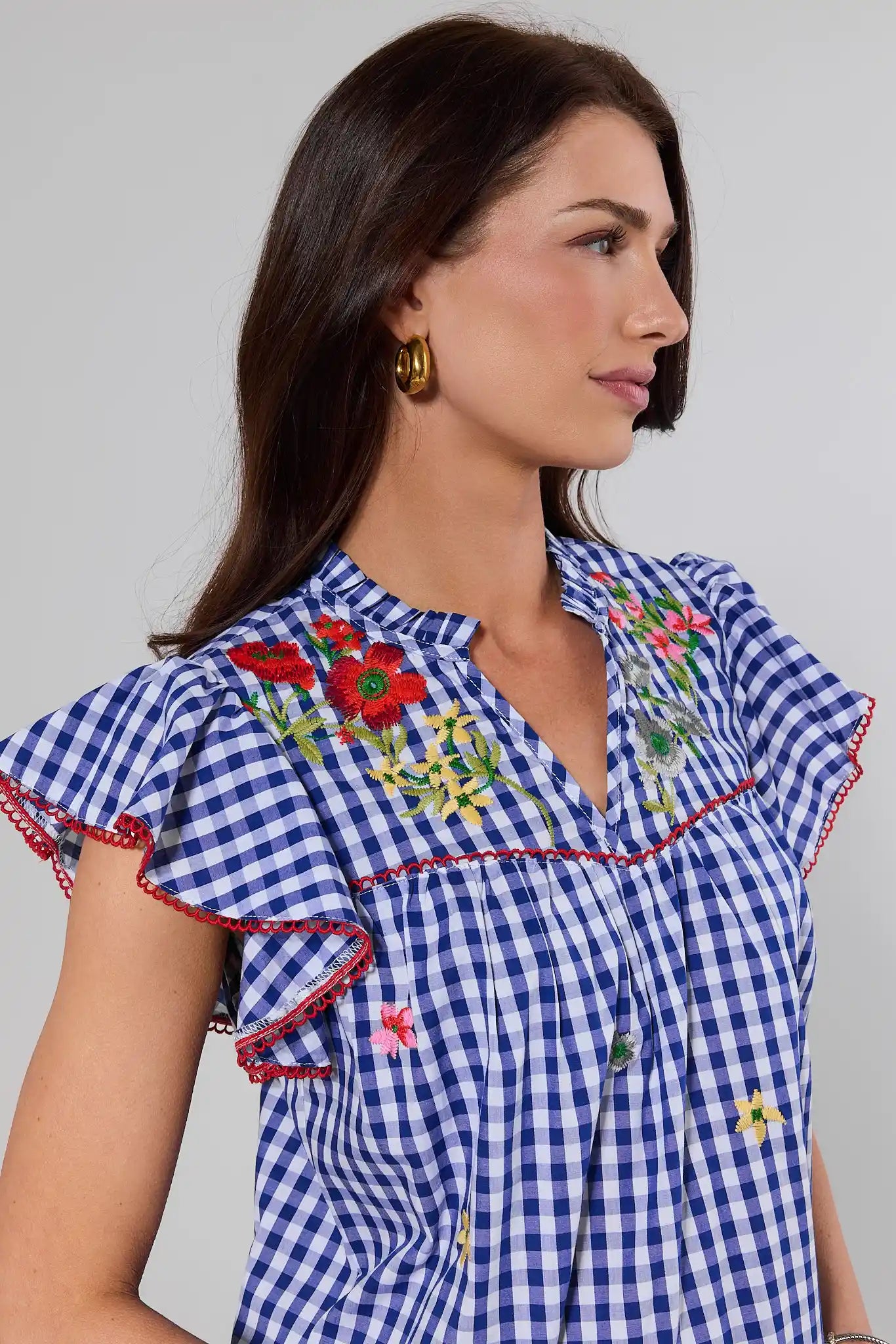 close up Woman wearing a blue checkered dress with floral embroidery against a plain background