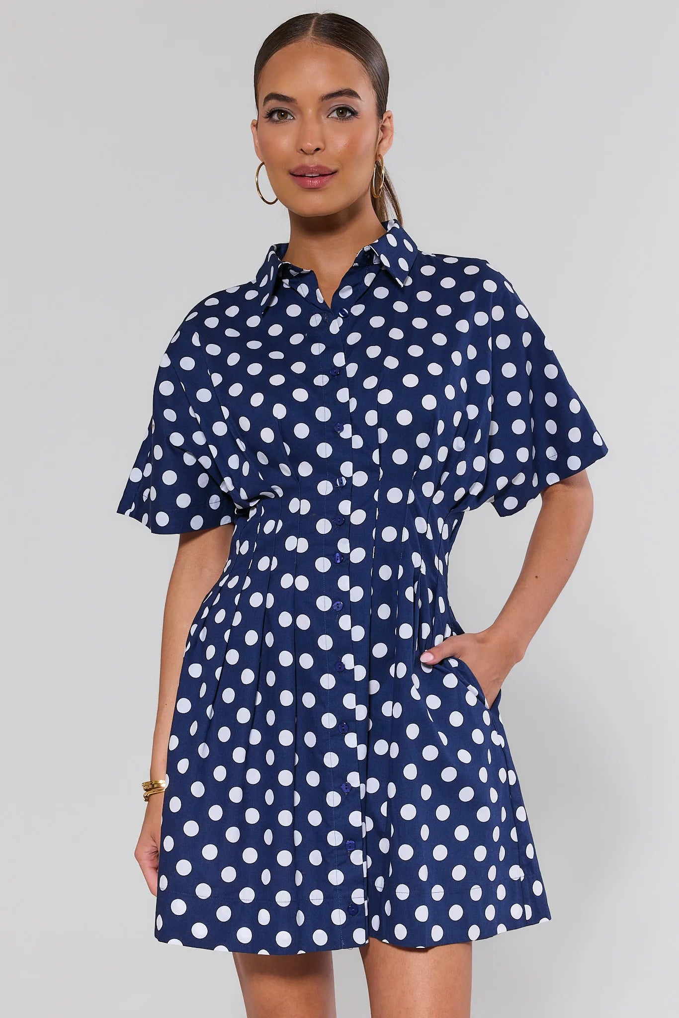 Woman wearing a navy blue dress with white polka dots on a plain background