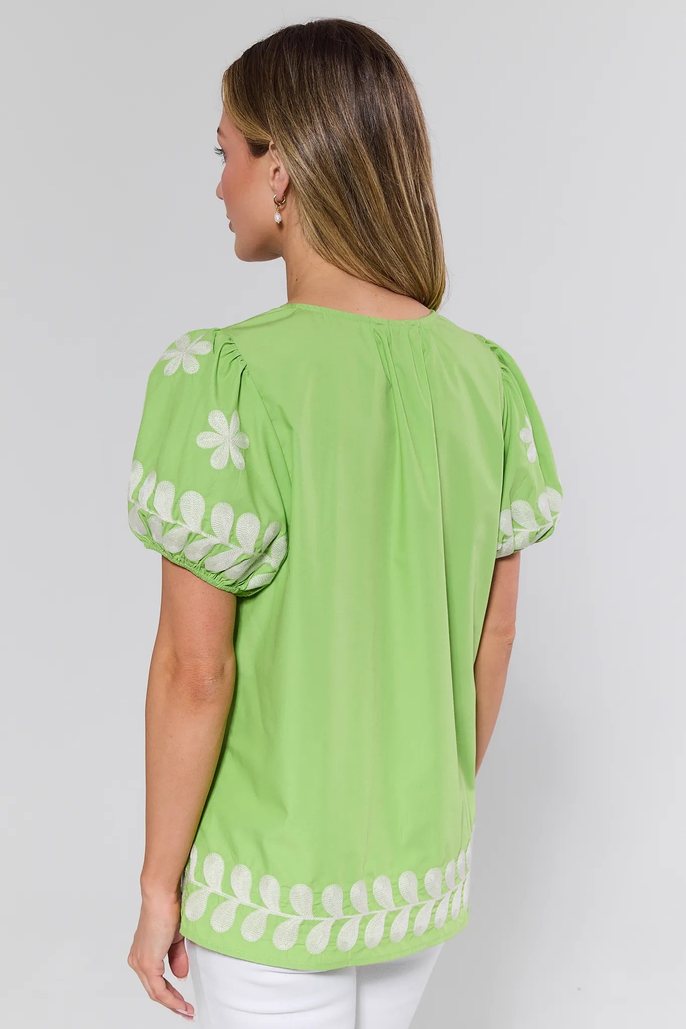 Woman wearing a green blouse with white floral patterns on a plain background