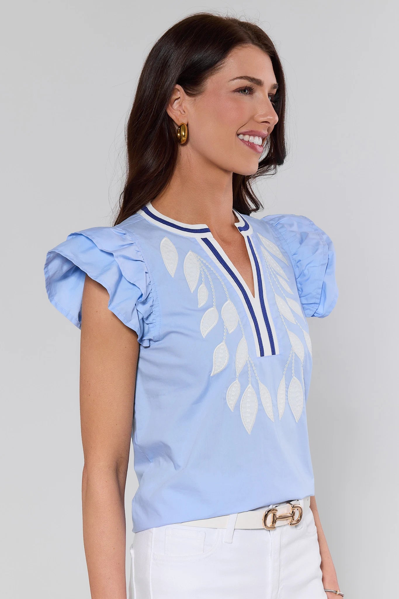side shot Woman wearing a light blue blouse with white leaf patterns on a plain background
