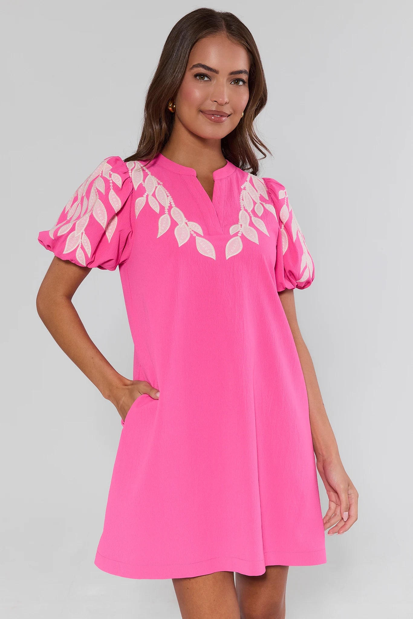 Woman wearing a pink dress with white floral embroidery on a gray background