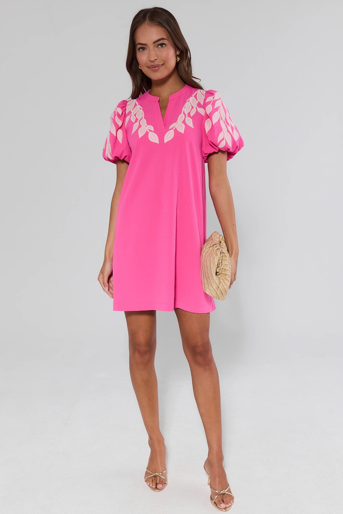 Woman wearing a bright pink Arianna dress with white floral patterns on a plain background