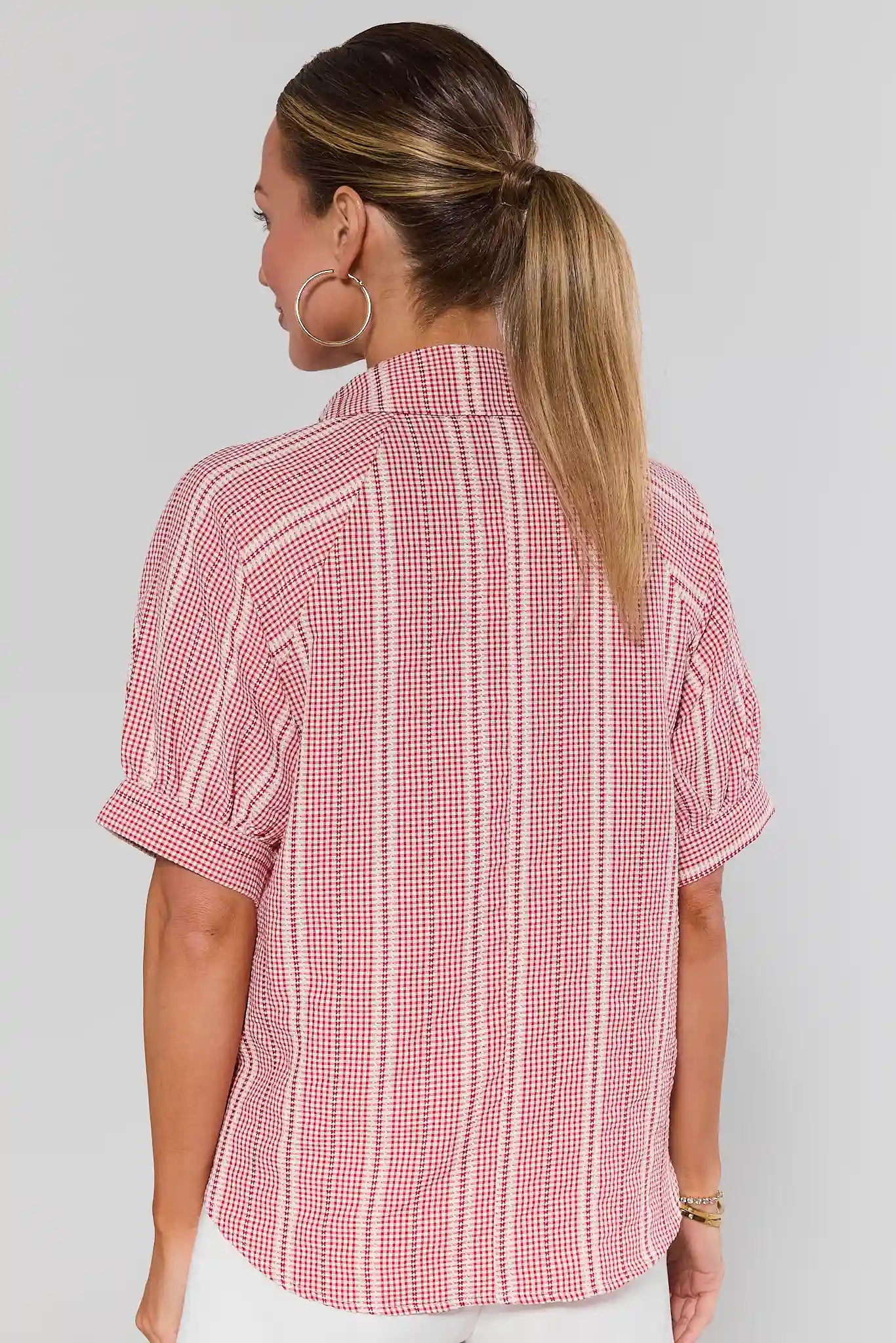 Woman standing wearing a red and white checkered shirt against a plain background