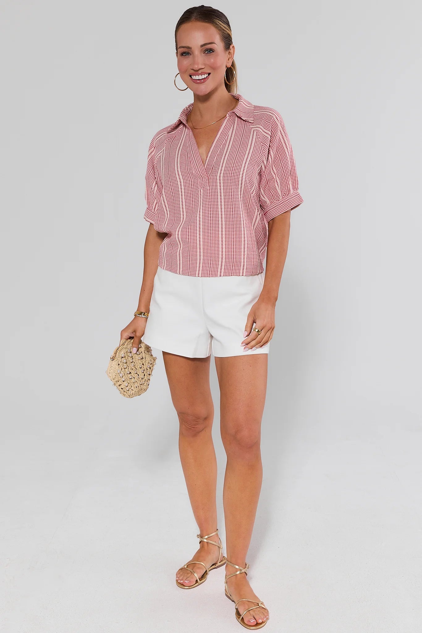 Woman wearing a pink striped shirt and white shorts on a gray background