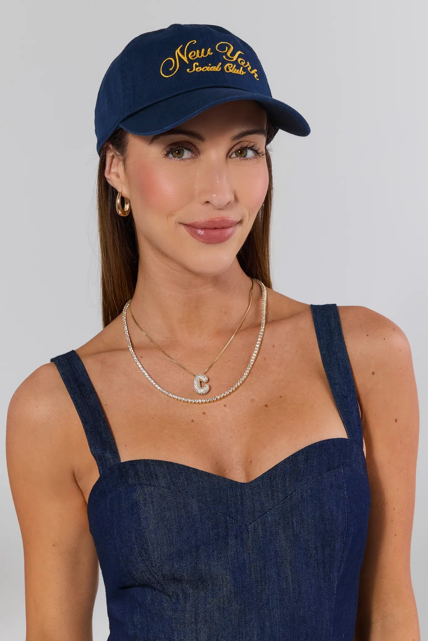 Woman wearing a navy cap with 'New York Social Club' text and a matching dress on a plain background