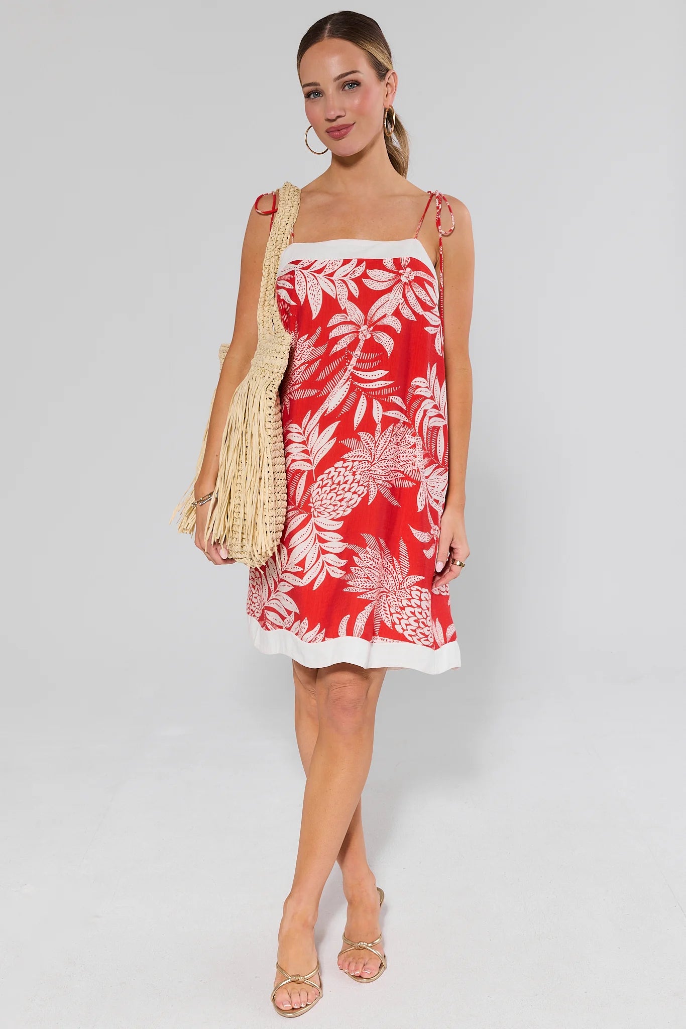 Woman wearing a red floral dress holding a straw bag on a white background
