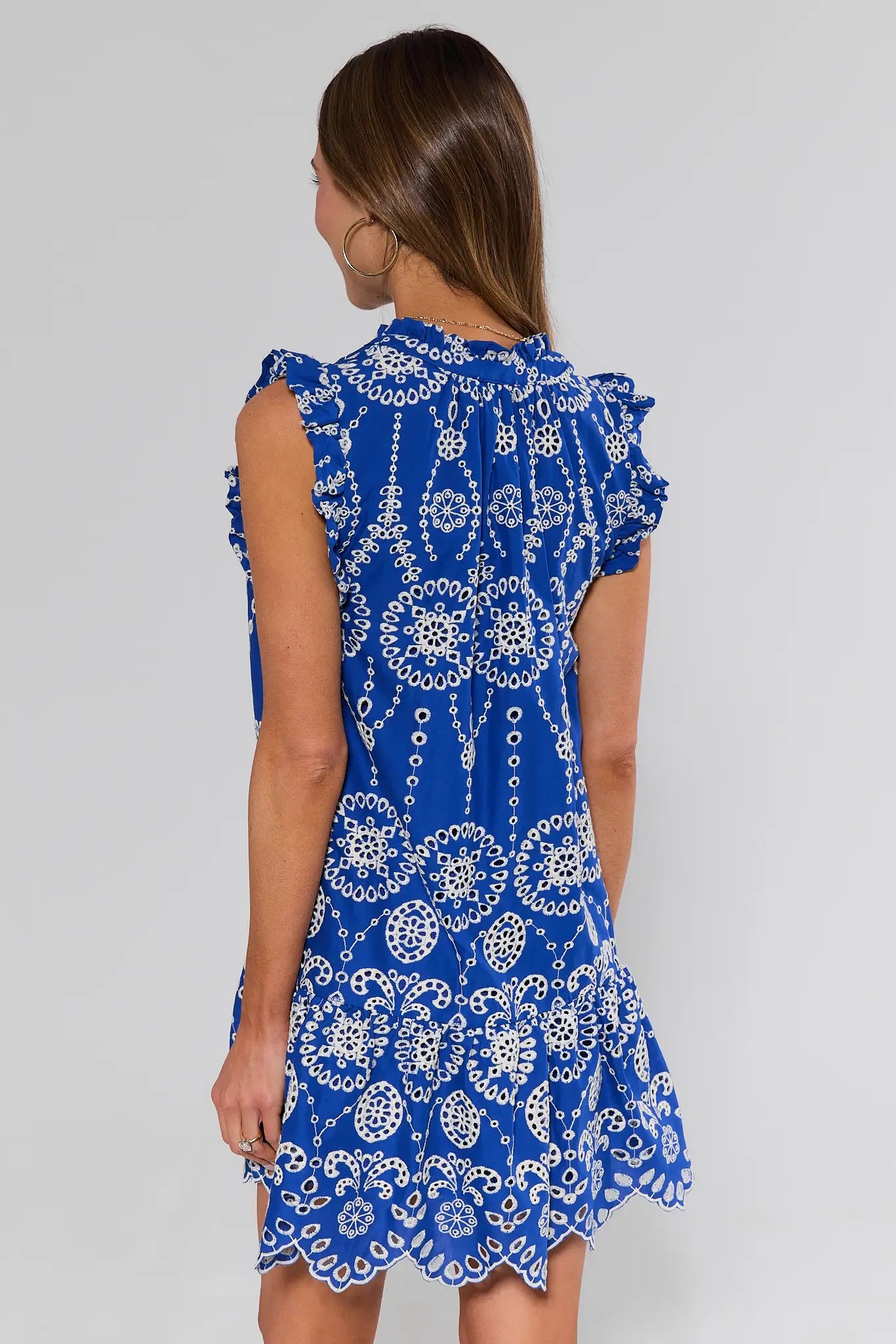 Woman standing wearing a blue and white patterned dress on a plain background