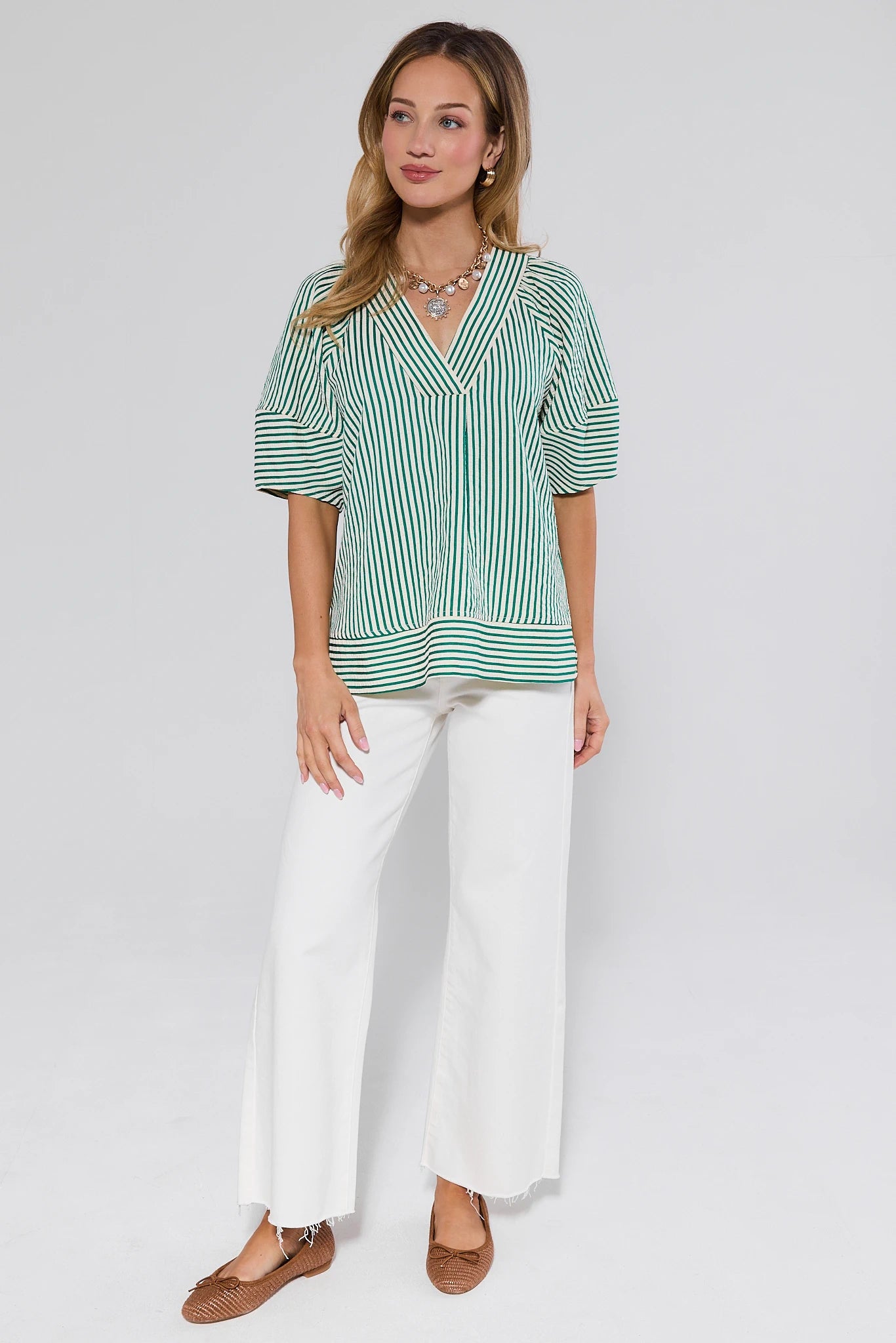 Woman wearing a green and white striped shirt with white pants on a plain background