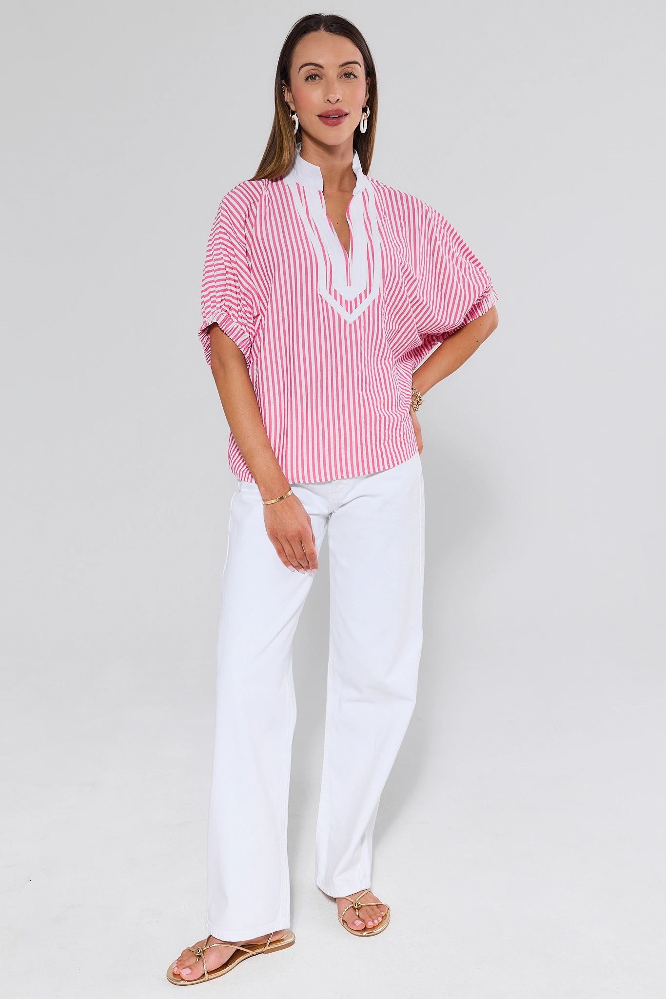 Woman wearing a red and white striped blouse with a white collar and white pants on a light gray background