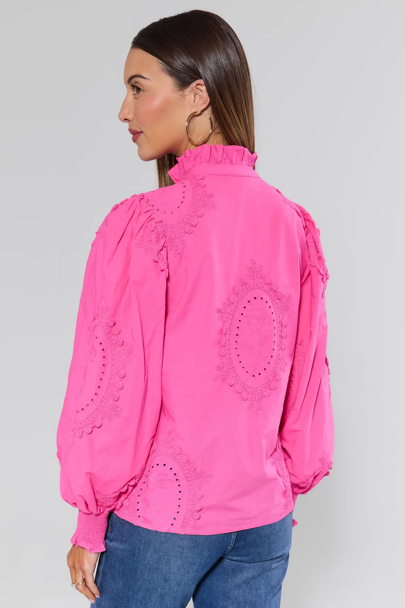 Woman wearing a bright pink blouse with intricate designs on a plain background