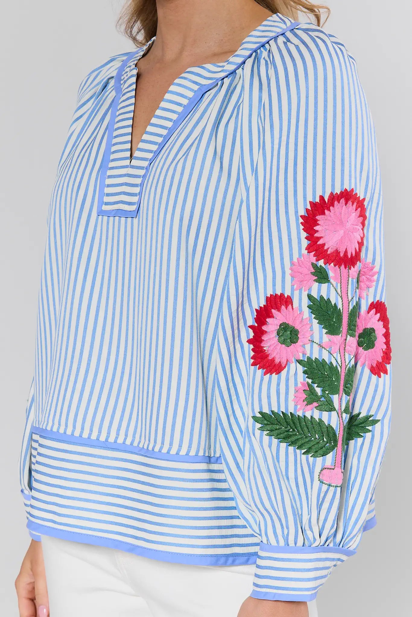 Blue and white striped top with floral embroidery on a plain background