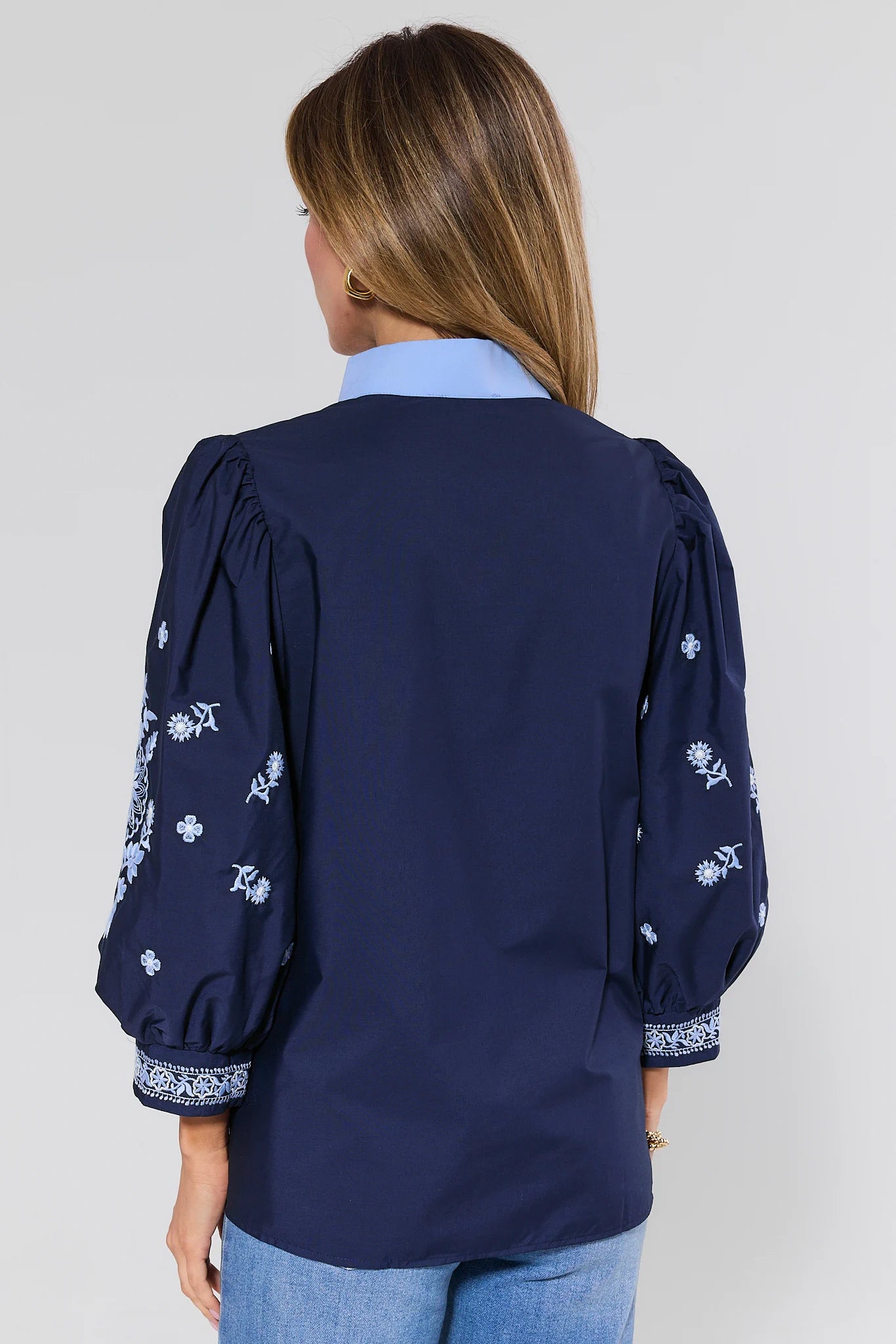 Navy blue blouse with floral patterns on long sleeves worn by a person against a plain background