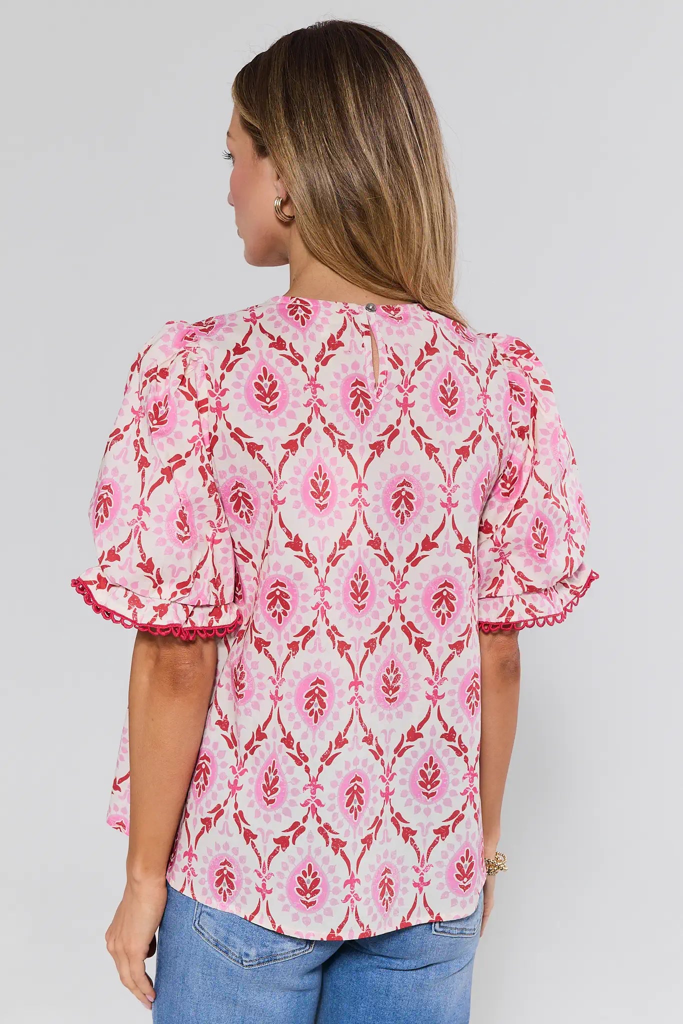 Woman wearing a pink floral blouse with ruffled sleeves on a plain background