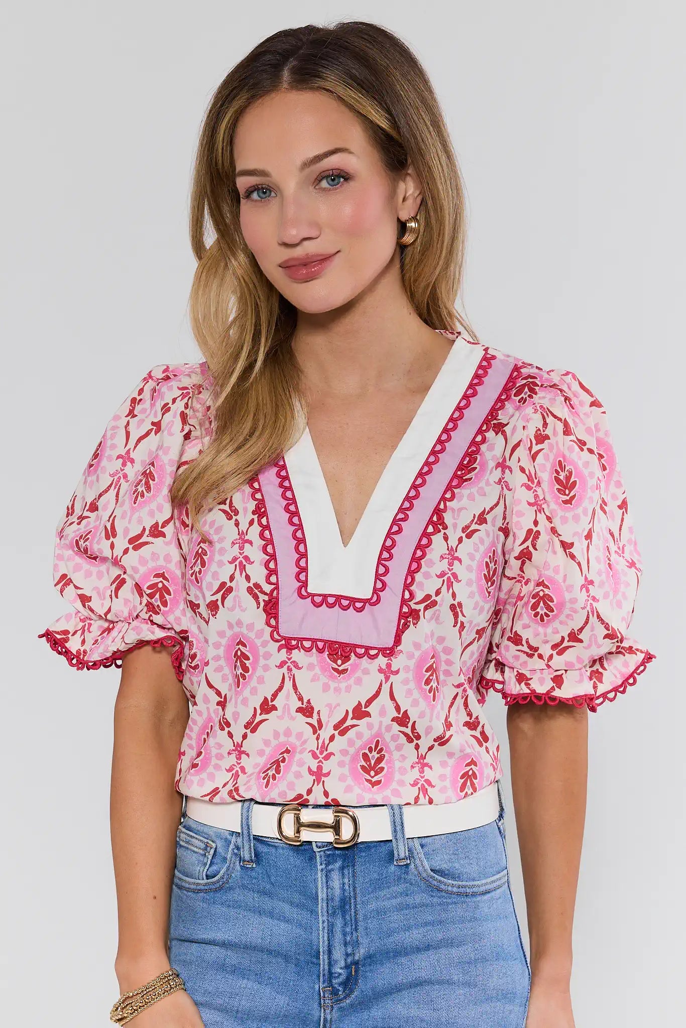 Woman wearing a pink floral blouse with white trim and blue jeans on a plain background