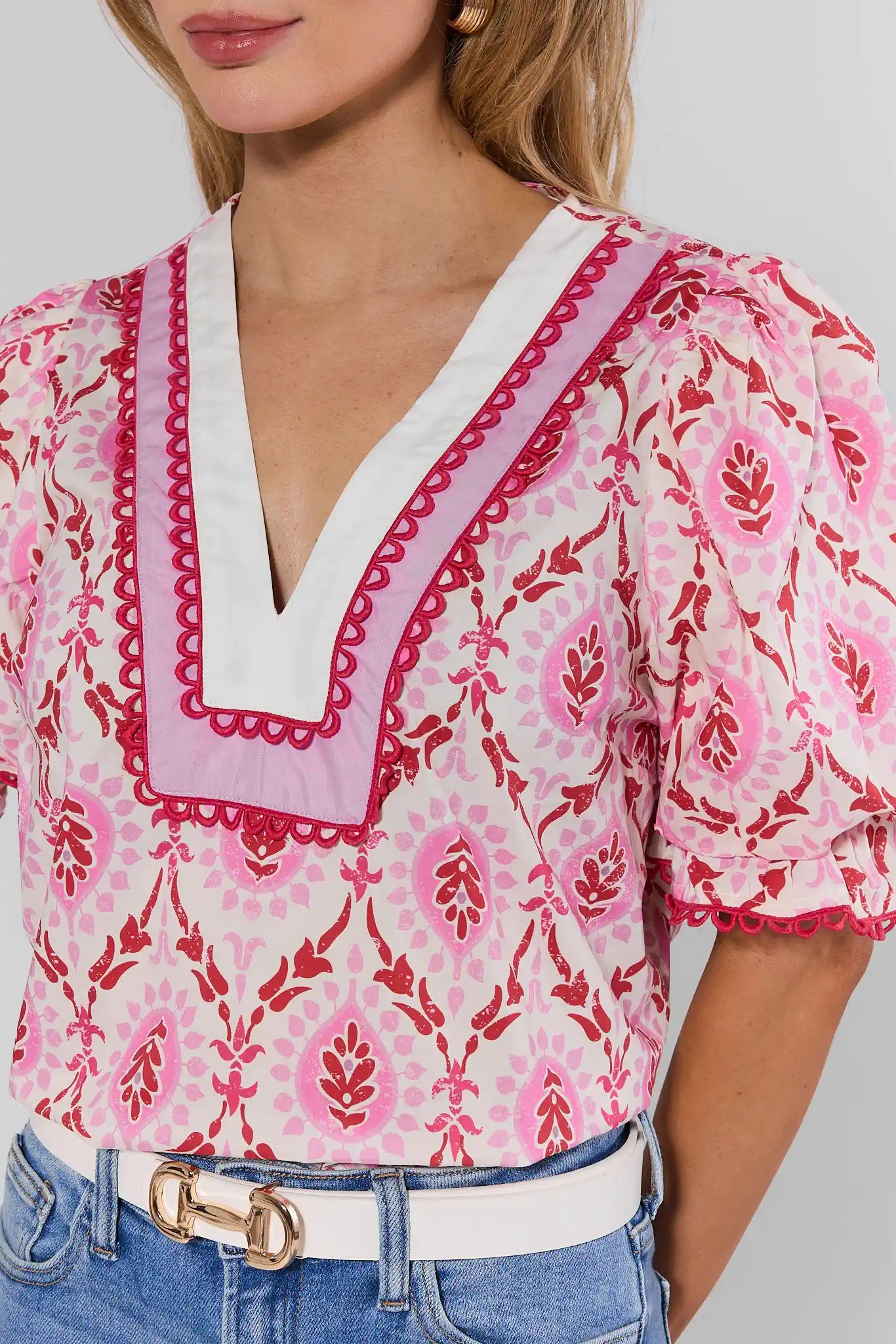 Woman wearing a pink and white patterned blouse with blue jeans on a plain background