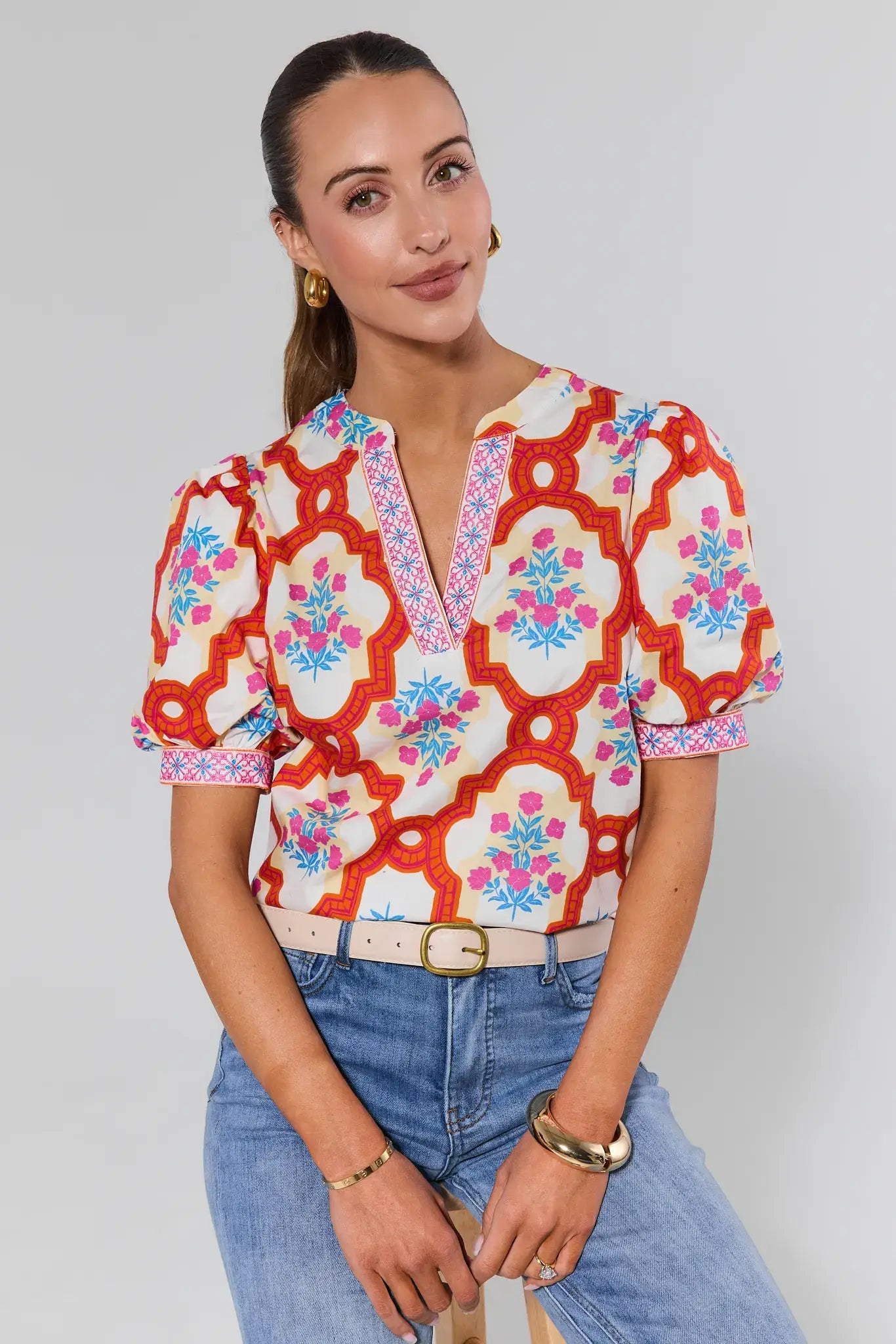 Woman wearing a colorful patterned blouse and blue jeans on a plain background