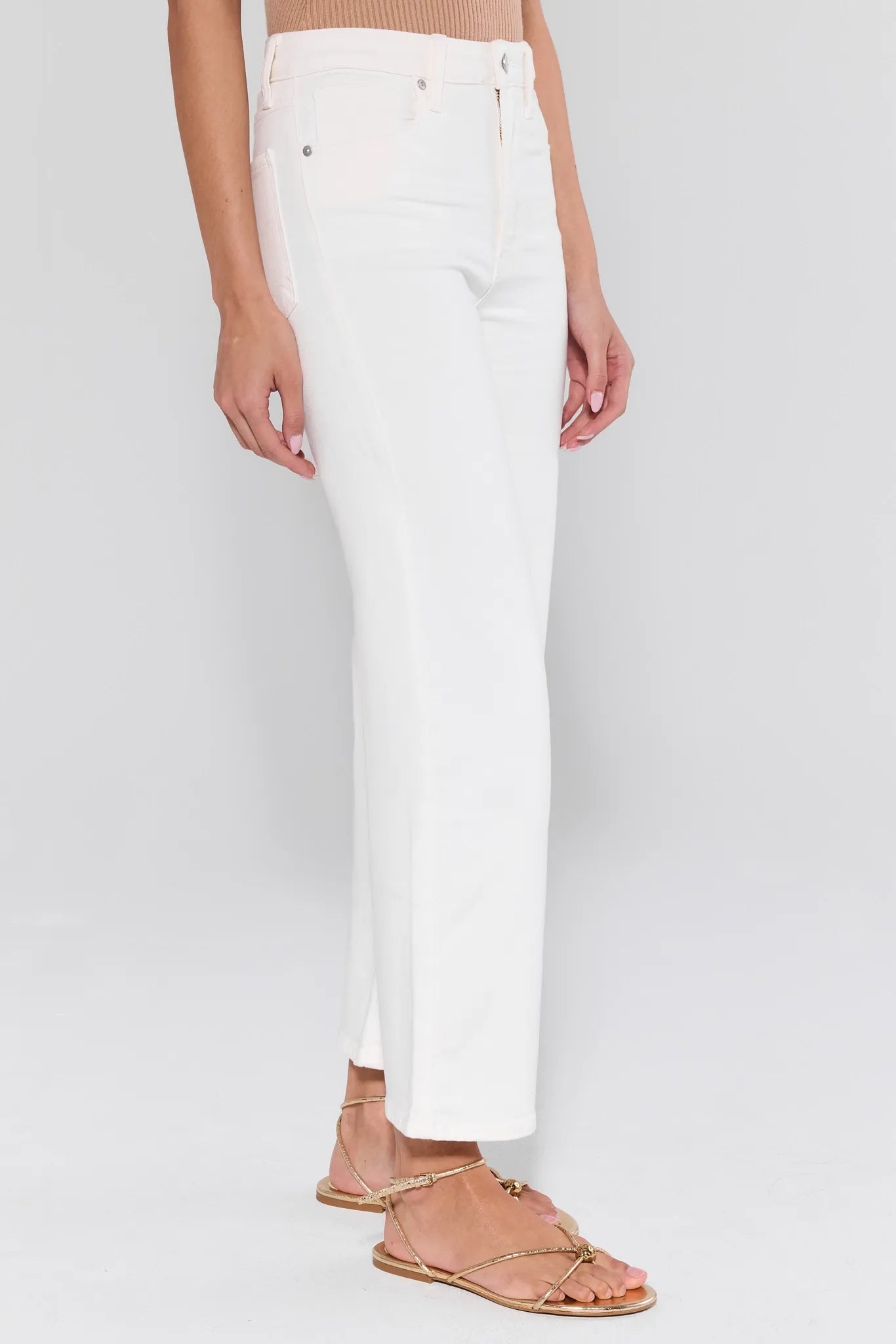 Person wearing white pants and tan sandals on a plain background