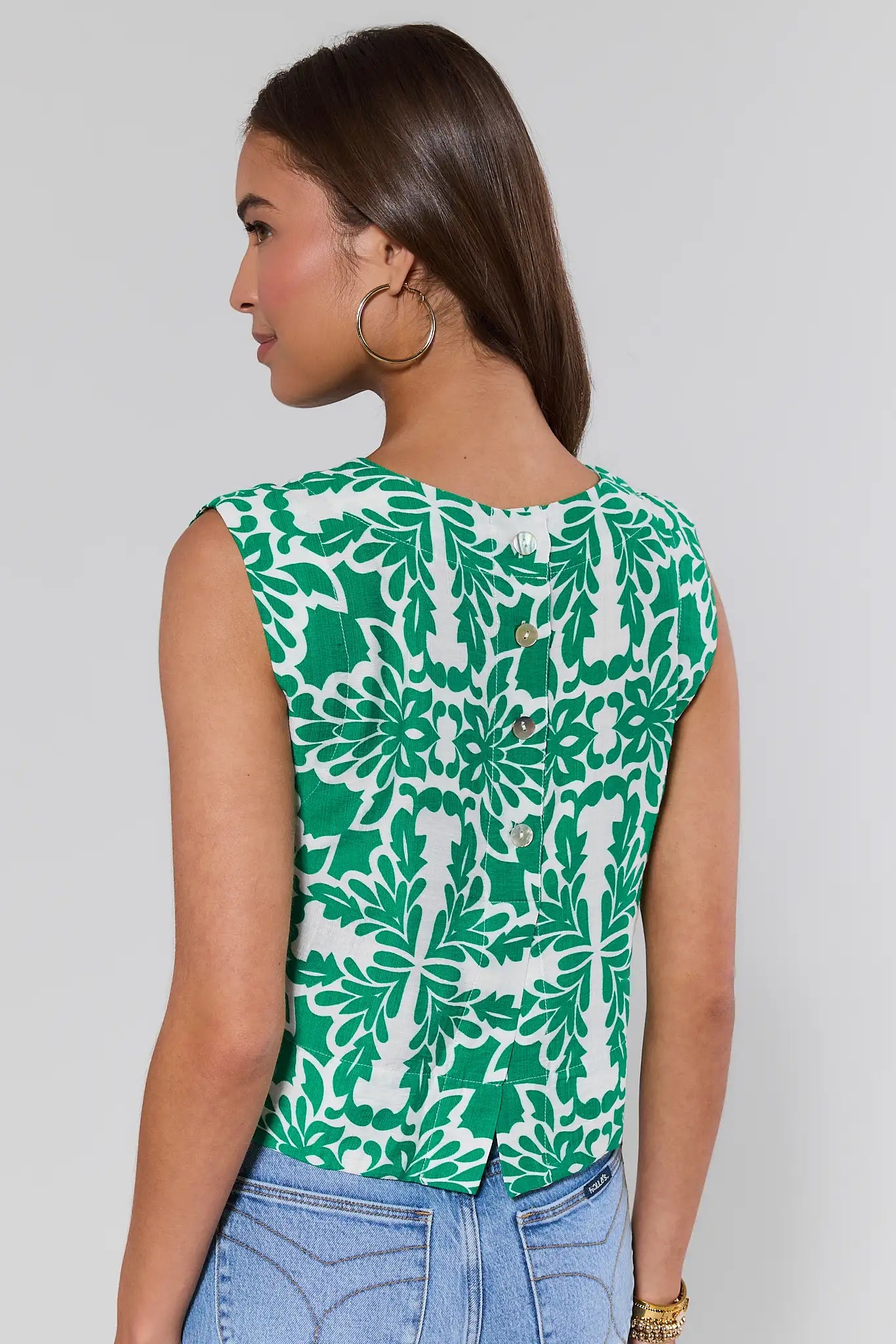 Woman standing wearing a green and white floral patterned top against a plain background