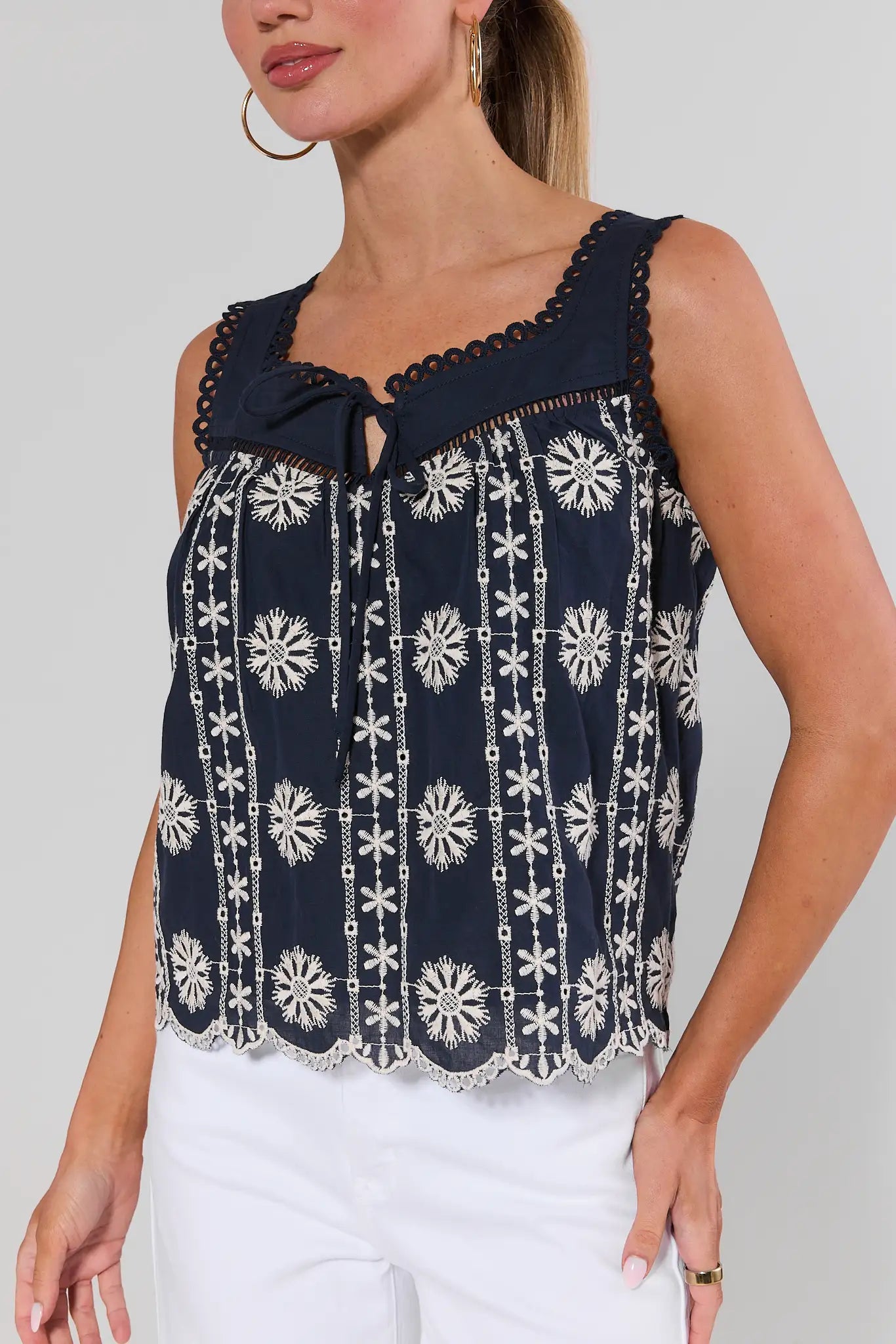 close up Woman wearing a navy sleeveless top with white floral patterns on a plain background