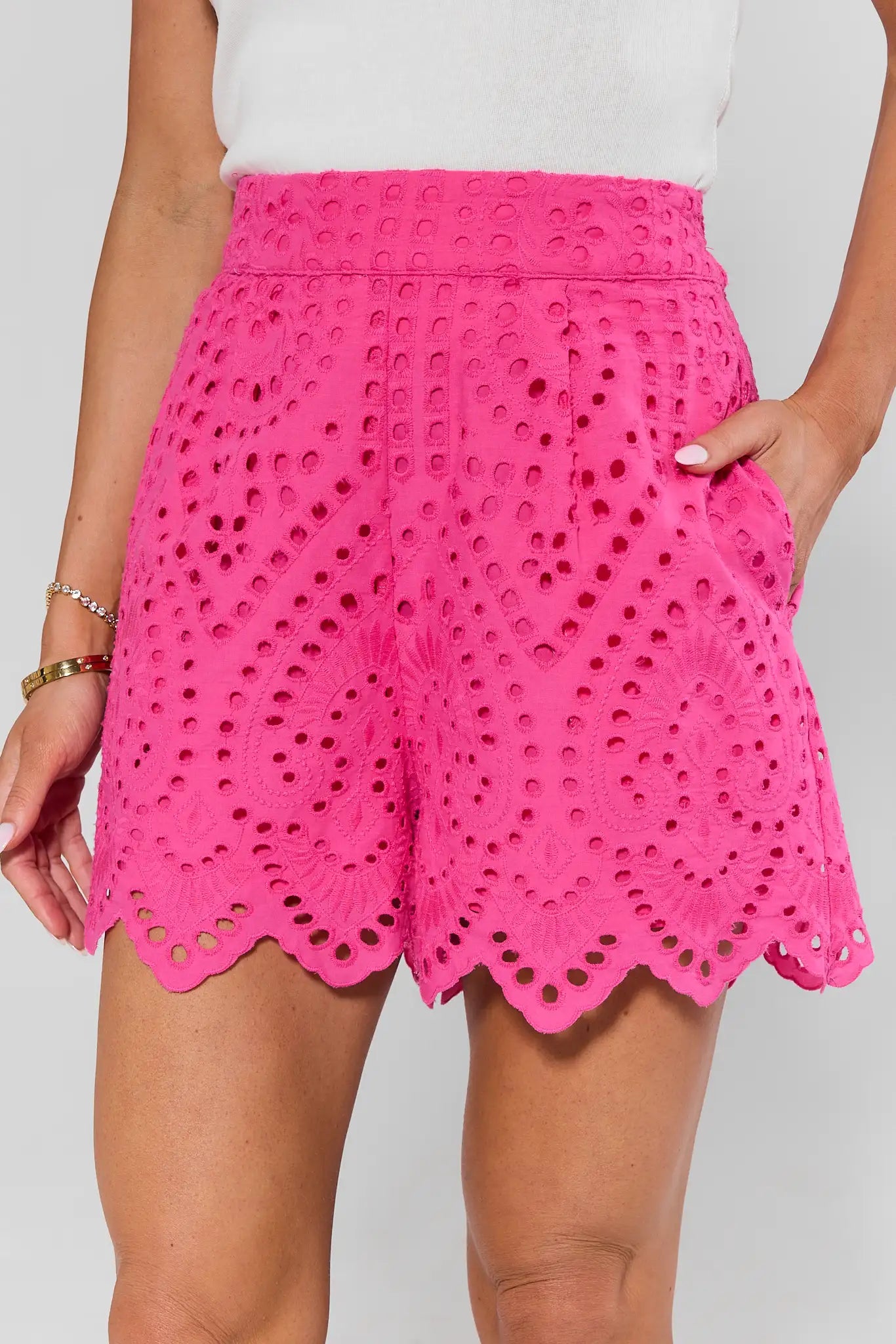 Person wearing bright pink eyelet shorts on a plain background