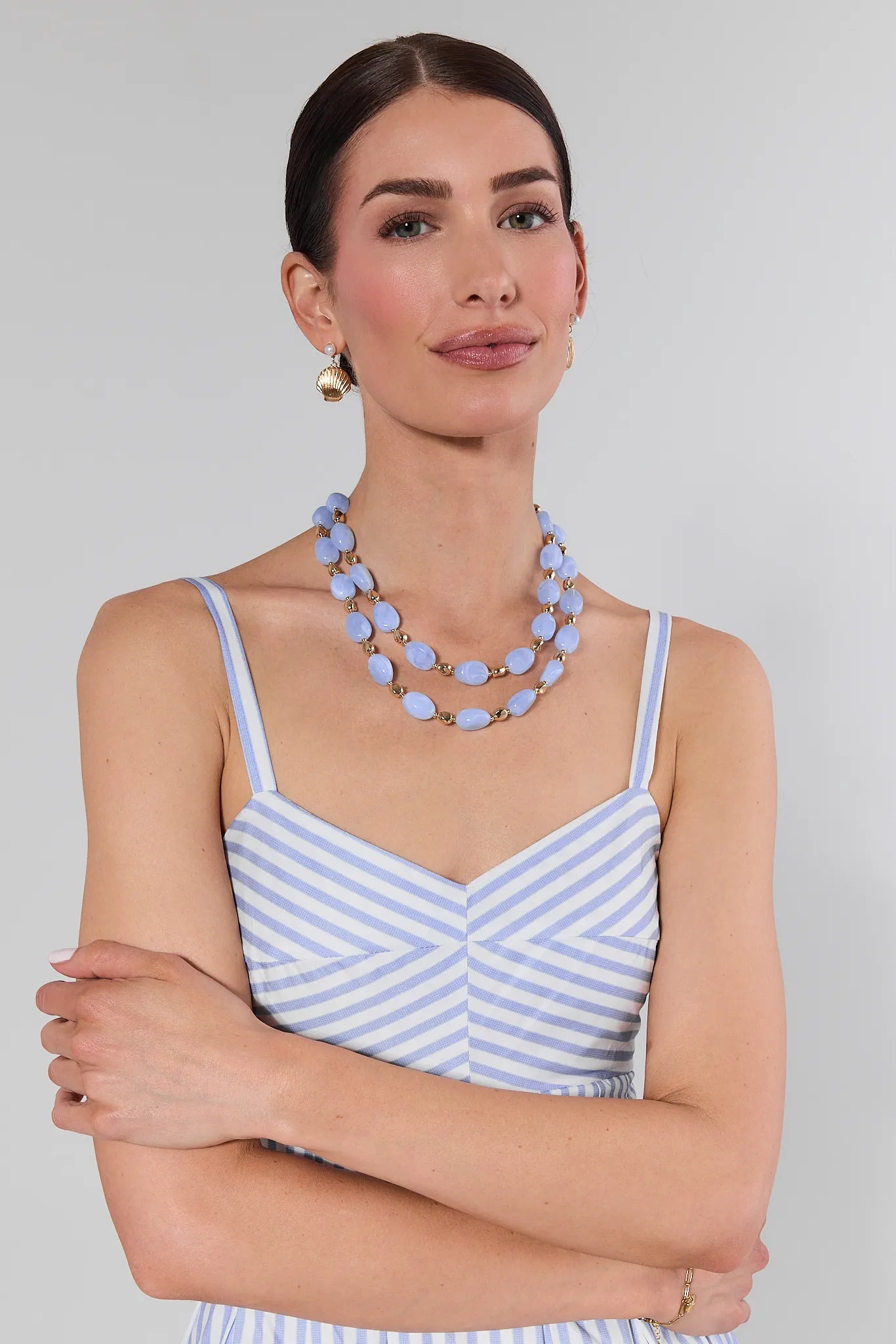 Woman wearing a blue and white striped dress with a layered necklace on a plain background