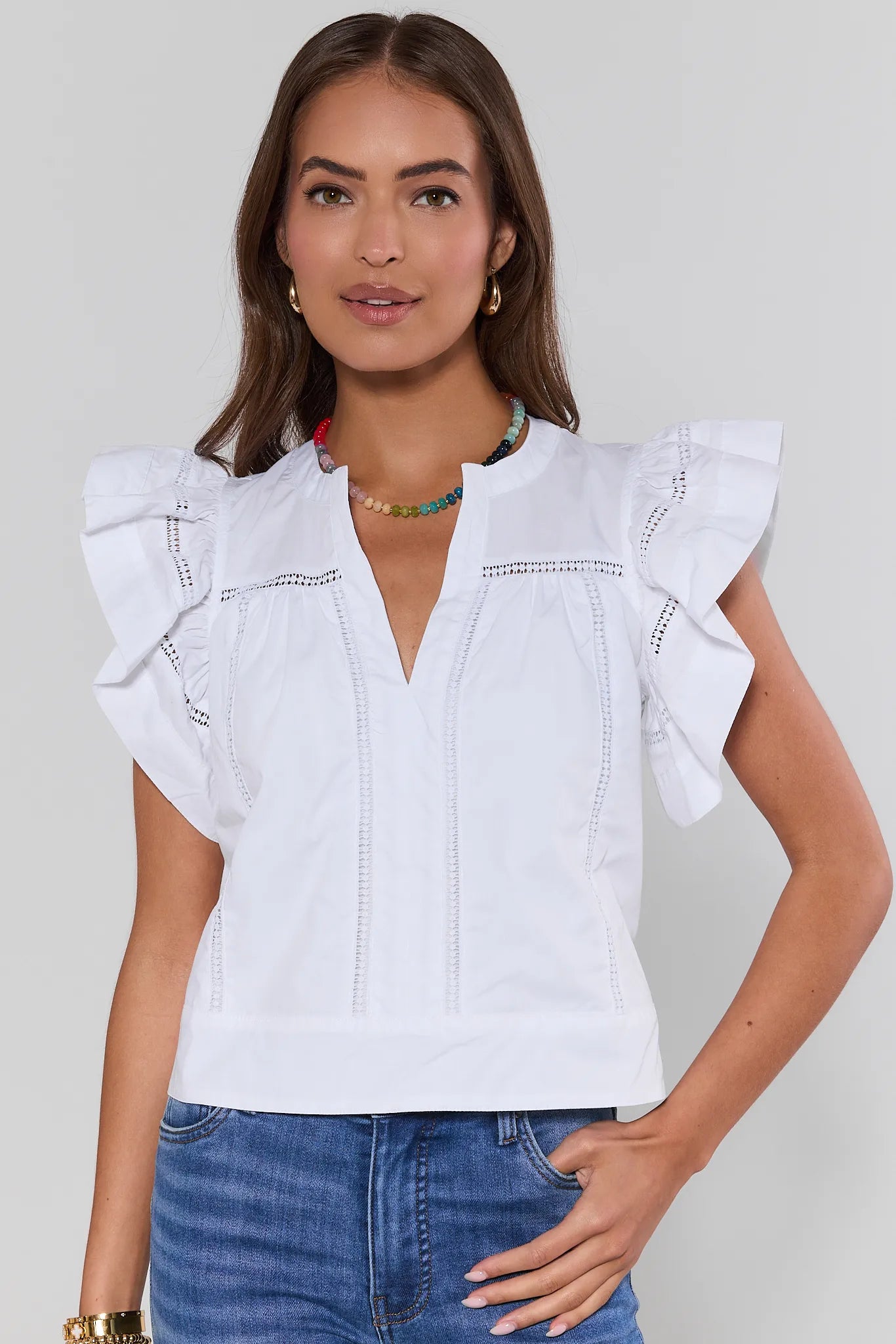 Woman wearing a white blouse with ruffled sleeves and blue jeans on a plain background
