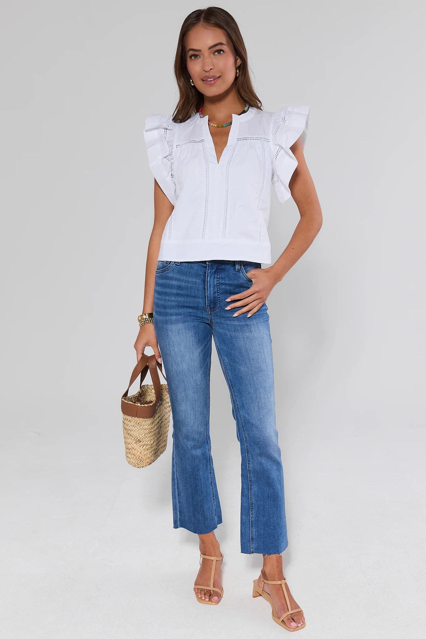 Woman wearing a white blouse and blue jeans, holding a straw bag on a plain background