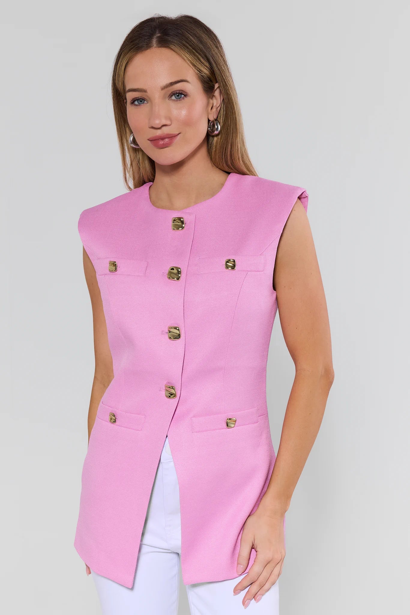 Woman wearing a pink sleeveless jacket with gold buttons on a white background