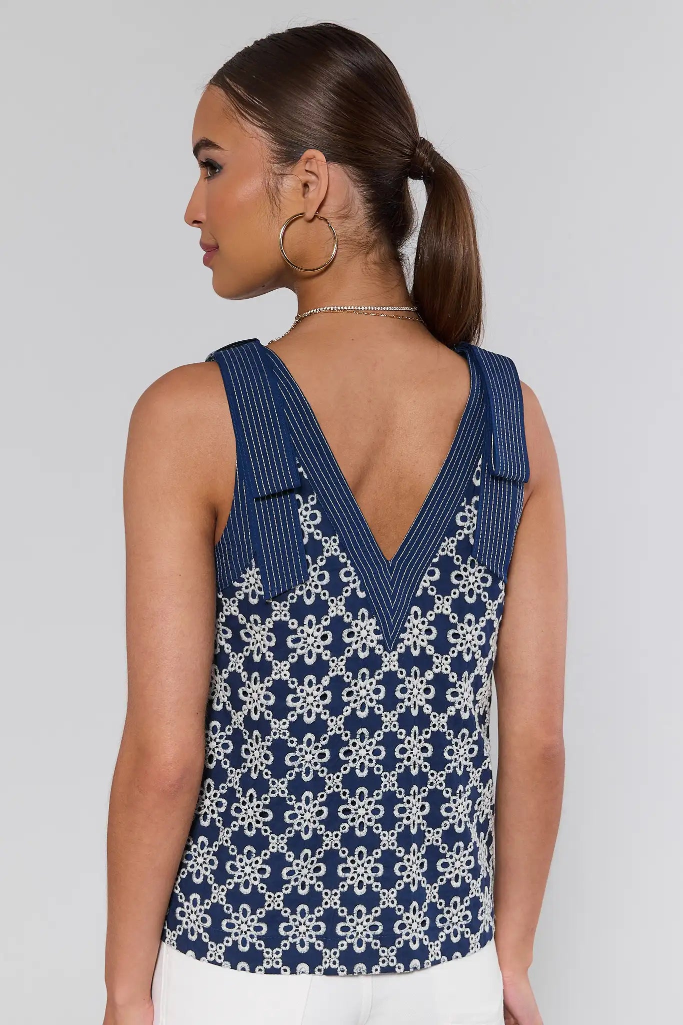 Woman standing wearing a blue sleeveless top with a white floral pattern on a plain background