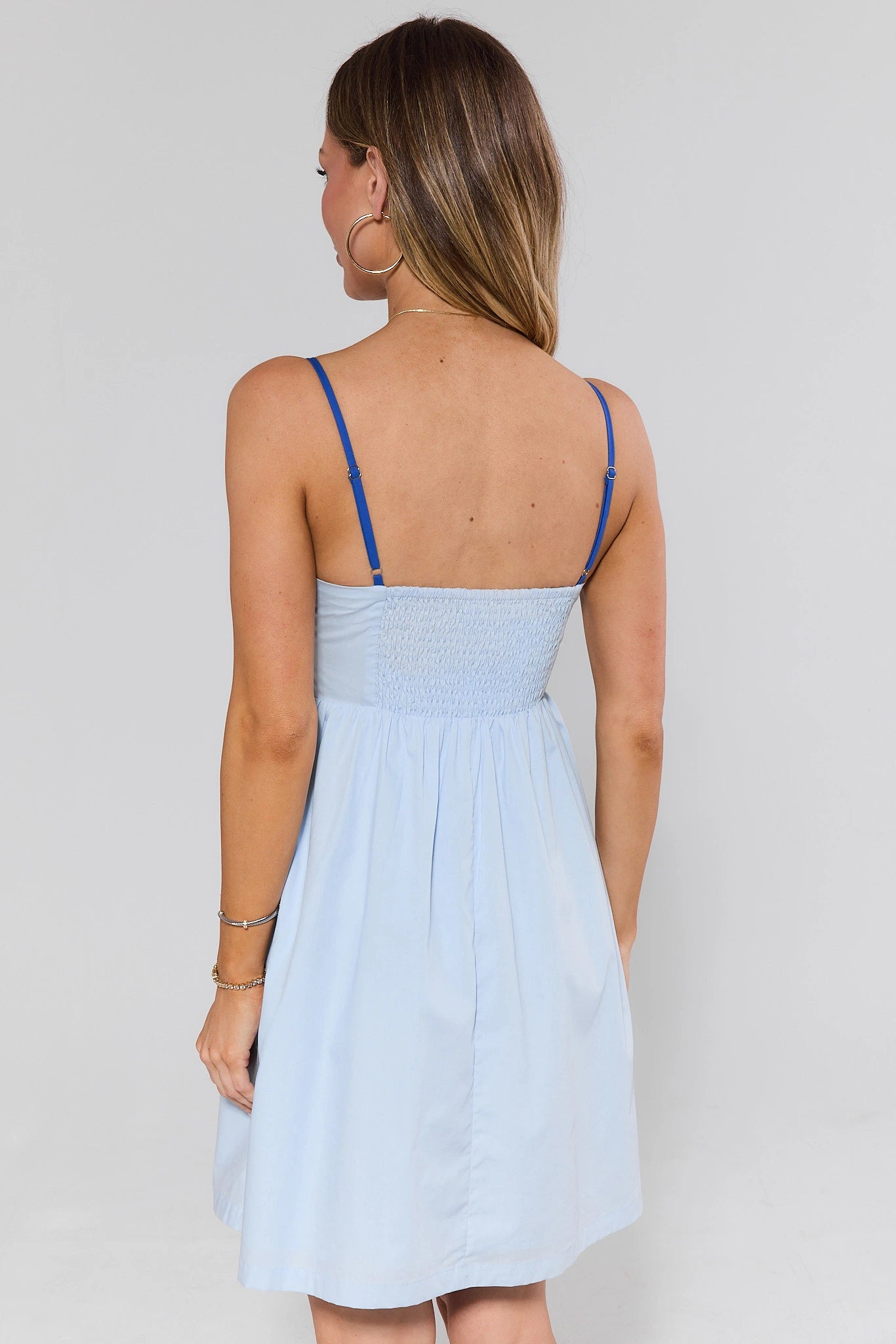 Woman standing wearing a light blue dress with thin straps against a plain background