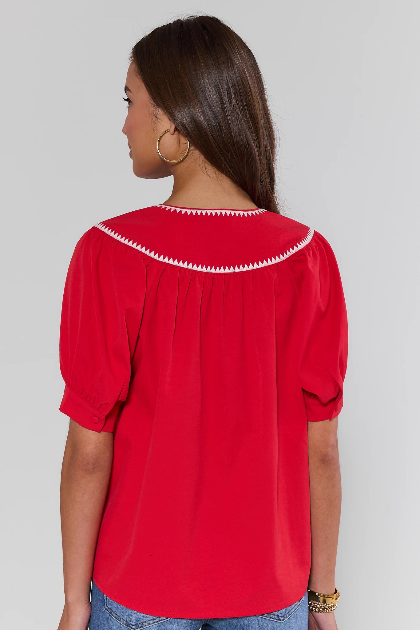 Woman standing wearing a red blouse with white trim on a plain background