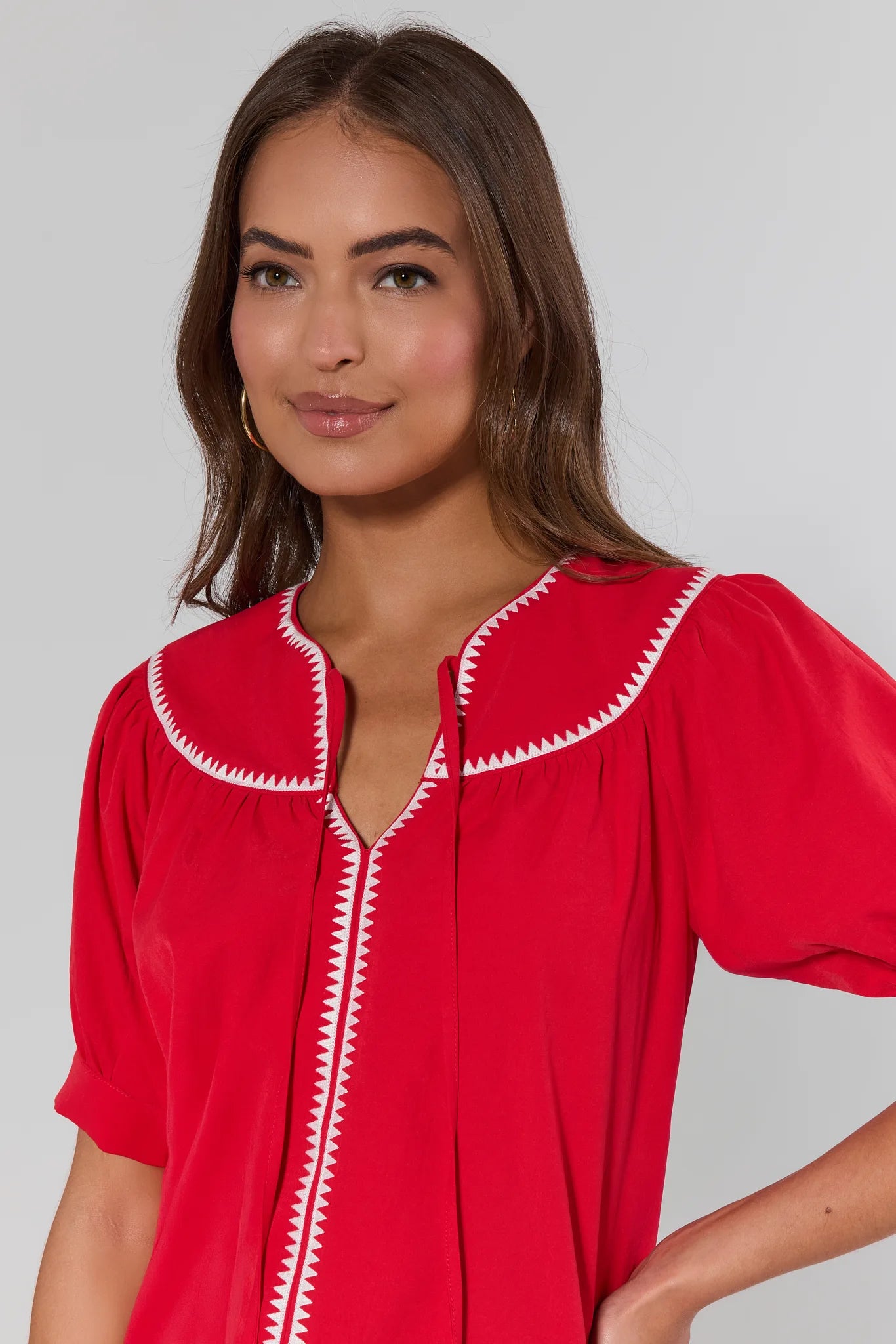 close up Woman wearing a red blouse with white trim against a gray background