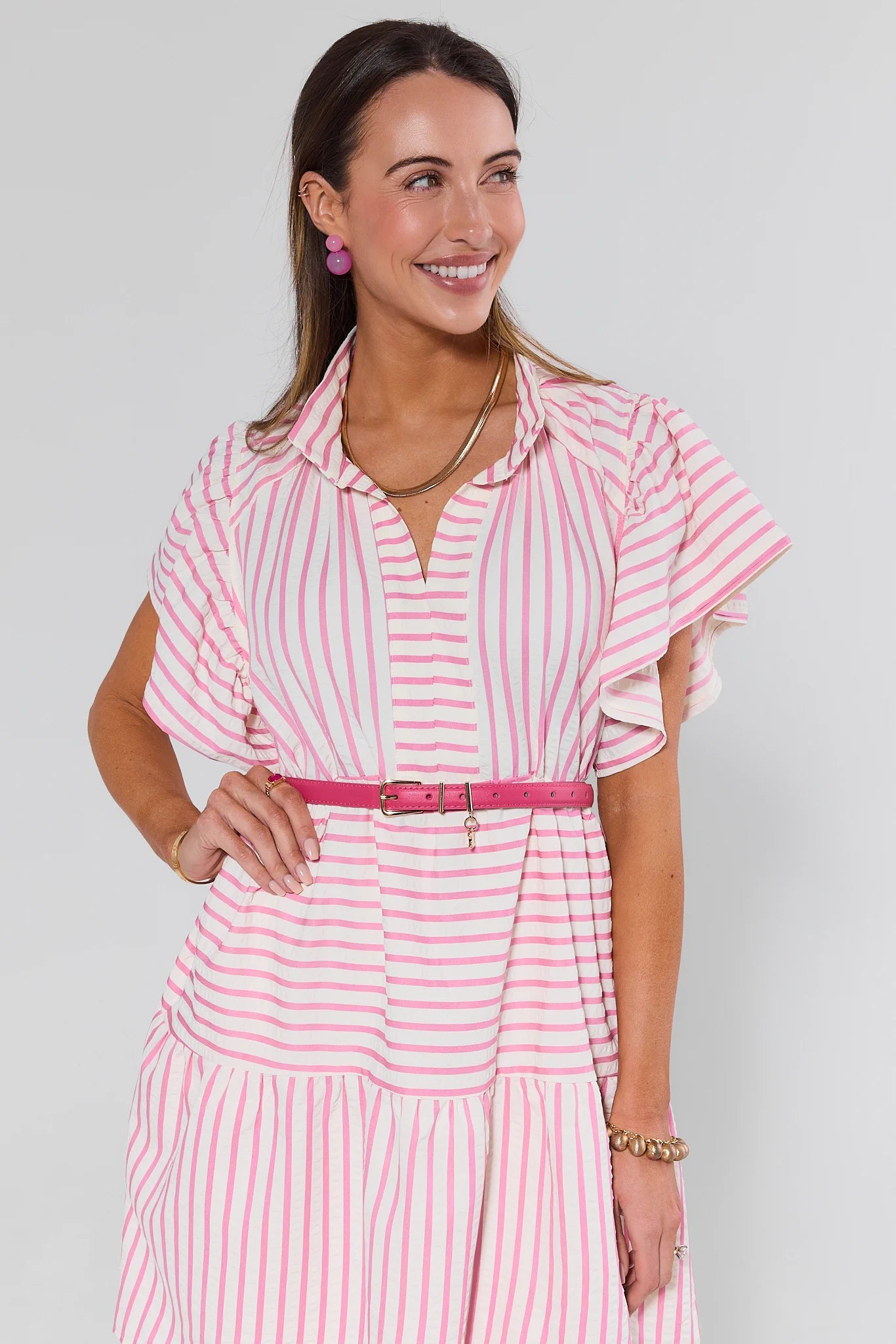 Woman wearing a pink and white striped dress with a belt on a gray background