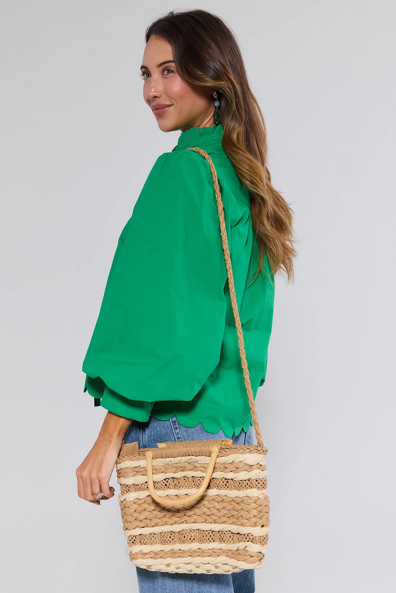 Woman wearing a green blouse and holding a straw bag against a gray background