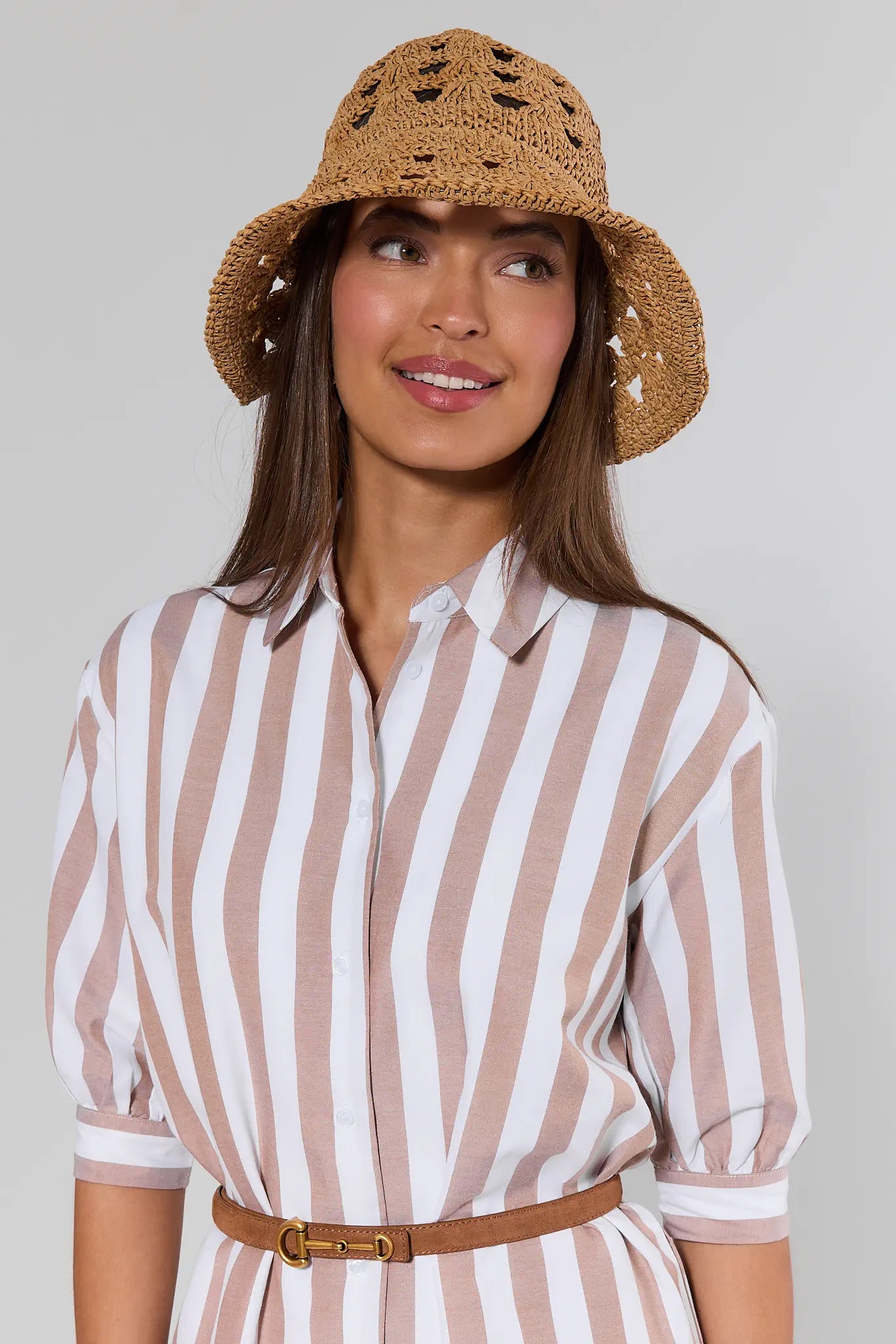 Woman wearing a striped shirt and straw hat against a plain background