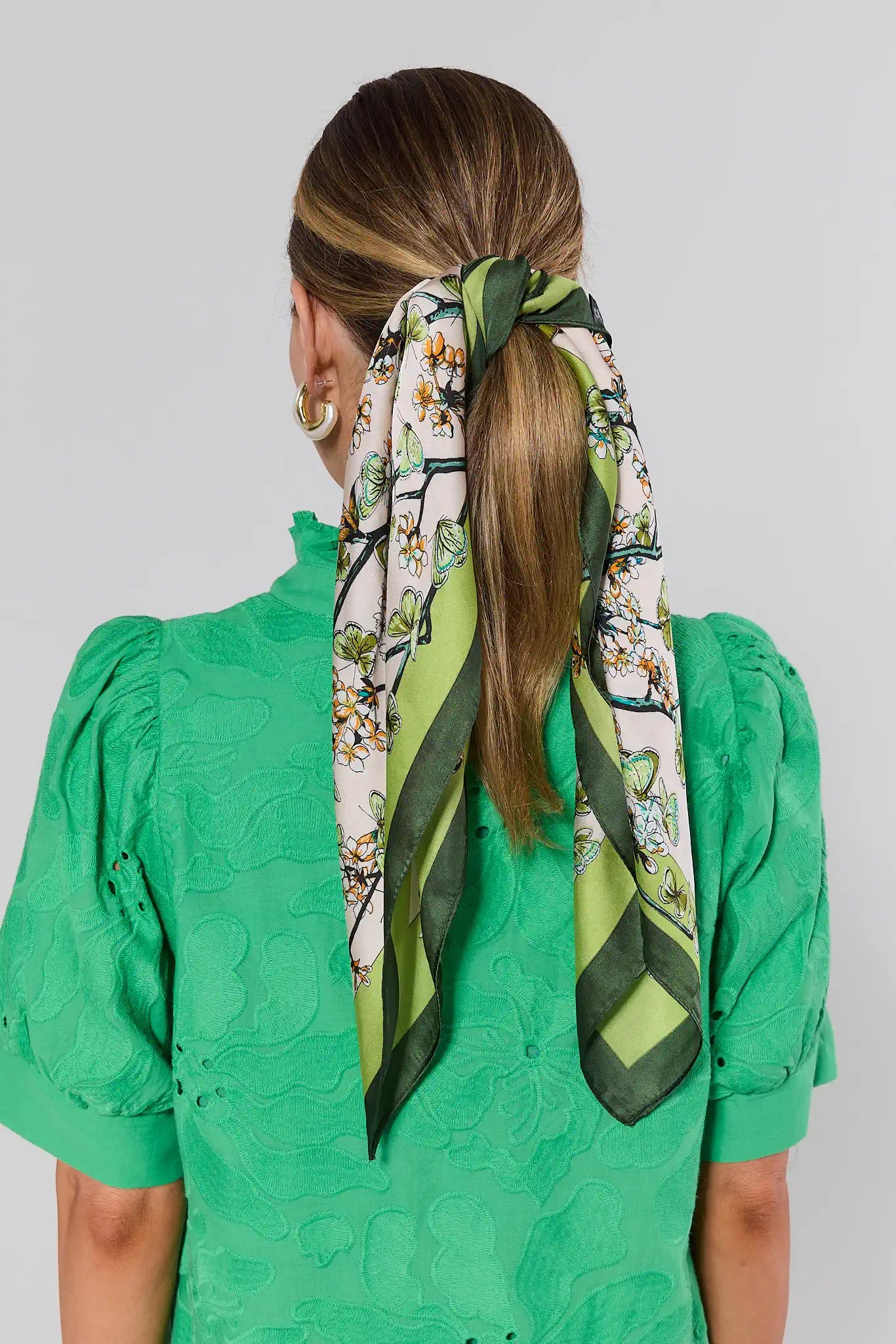 Woman wearing a green floral scarf tied around her hair with a plain background