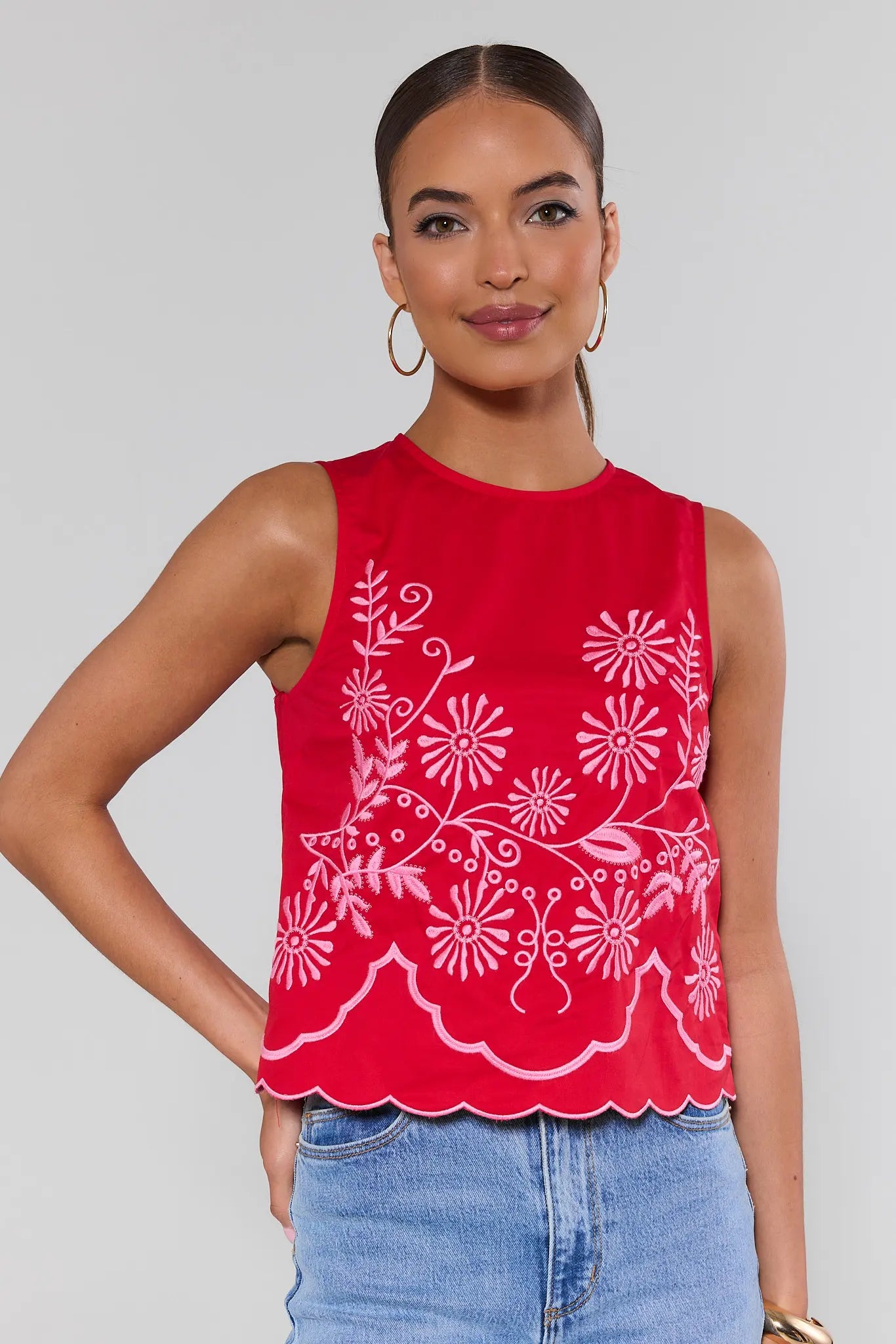 Woman wearing a red sleeveless top with white floral patterns on a plain background