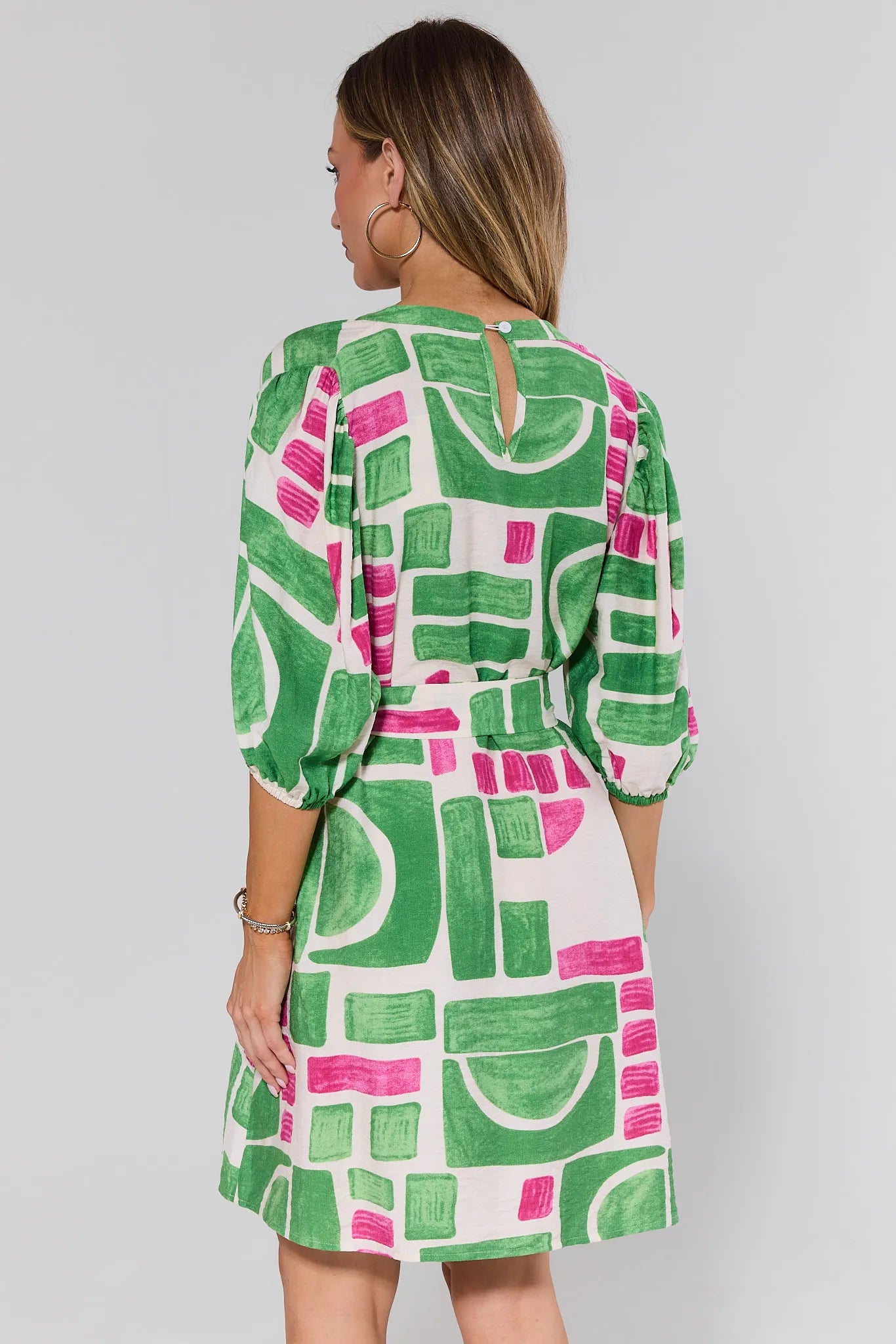 Woman standing wearing a green and pink patterned dress on a plain background