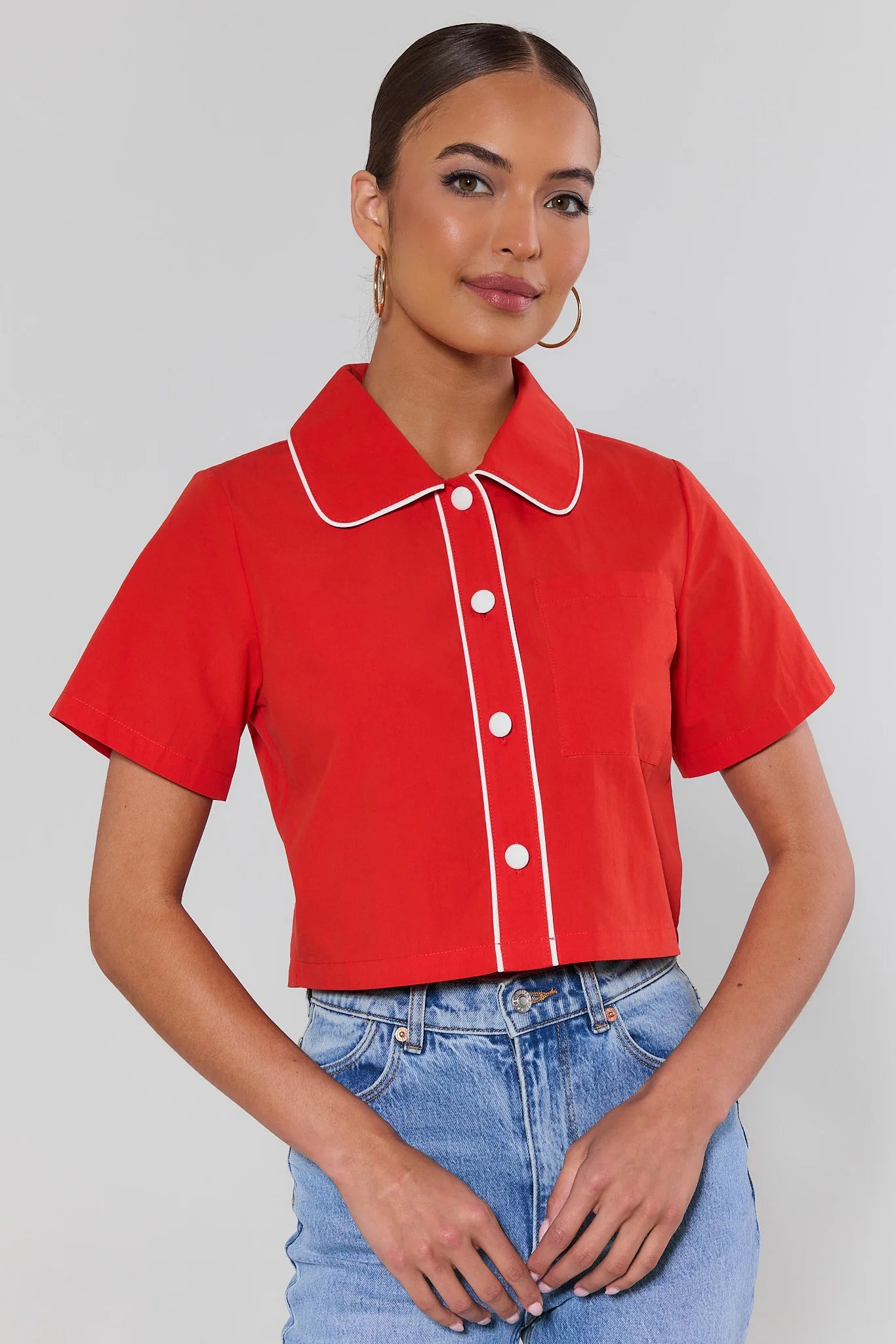 Woman wearing a red shirt with white trim and blue jeans on a gray background