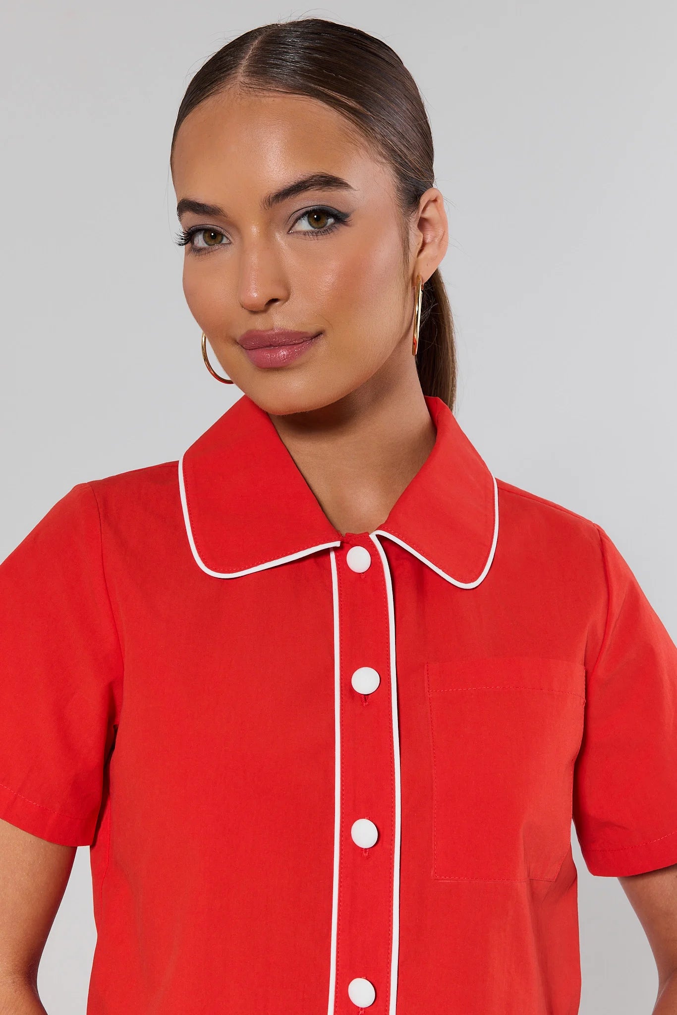 close up Woman wearing a red shirt with white trim against a gray background