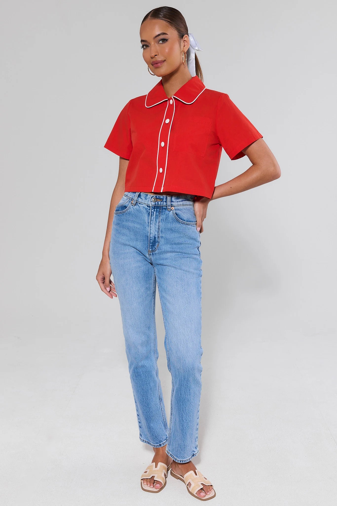 Person wearing a red cropped shirt with white trim and light blue jeans on a gray background